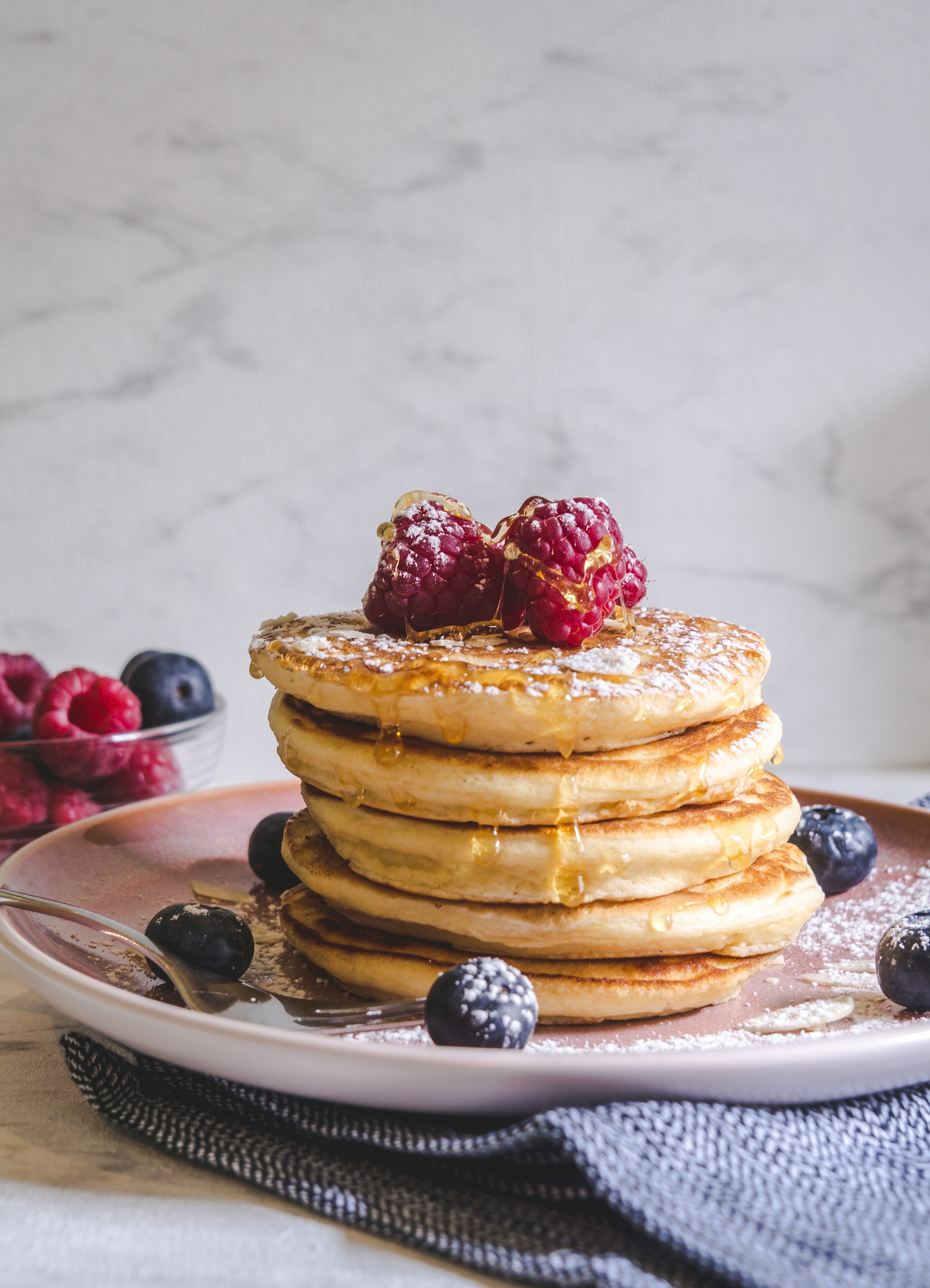 Ein Foto, das Pfannkuchen mit Beeren auf einem weißen Keramikteller zeigt | Quelle: Unsplash