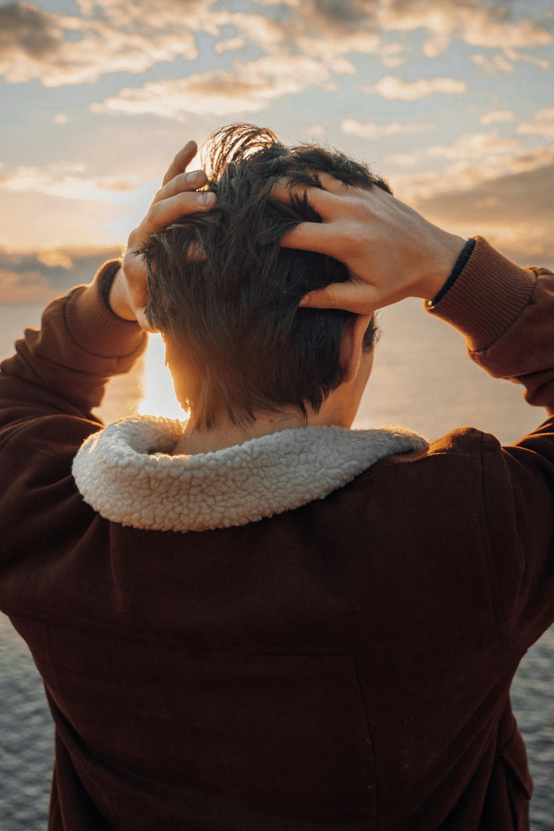 Ein Jugendlicher berührt seinen Hinterkopf, während er am Strand steht | Quelle: Pexels