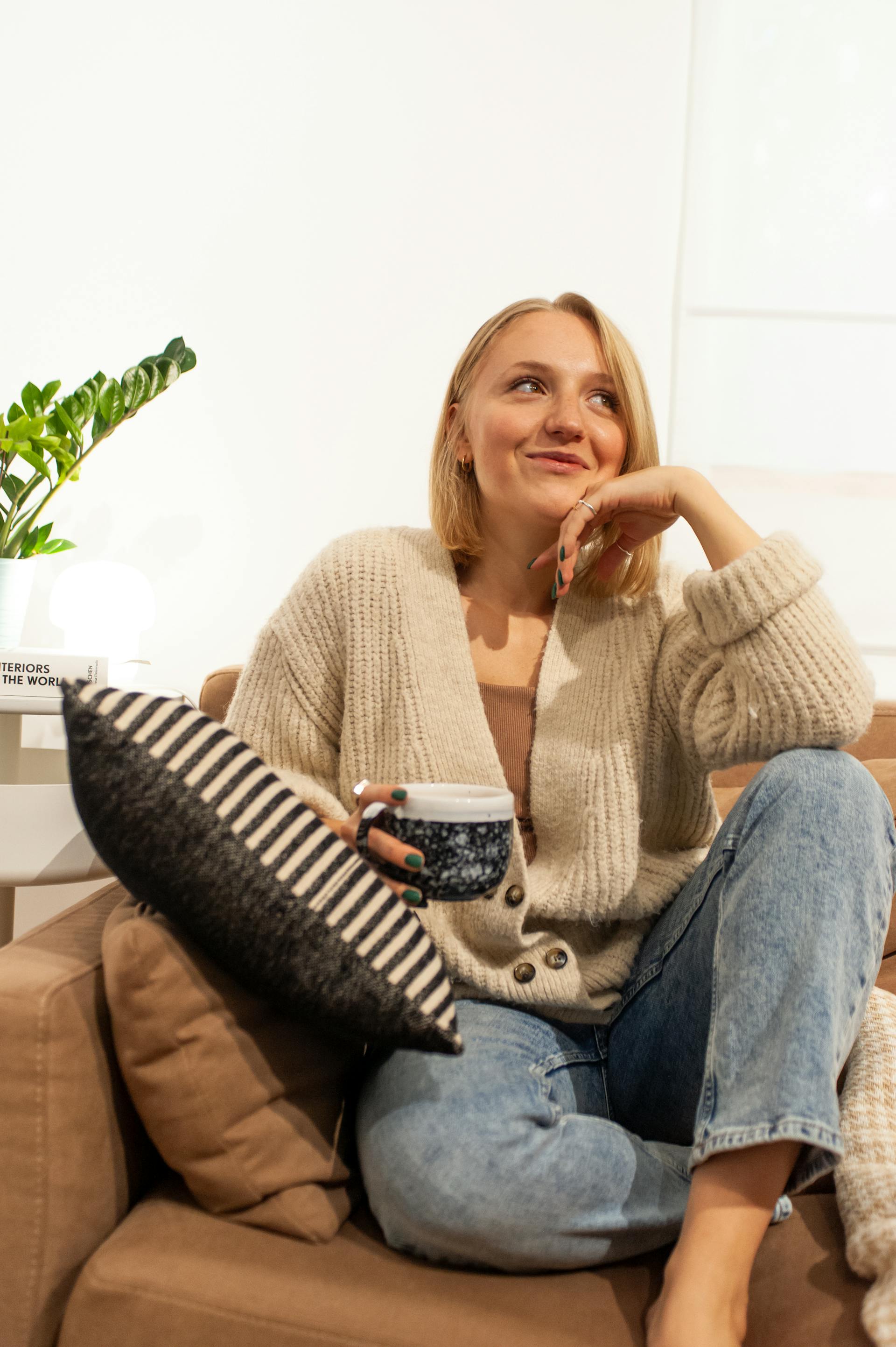 Eine lächelnde Frau sitzt auf einem Sofa und hält eine Tasse Kaffee in der Hand | Quelle: Pexels