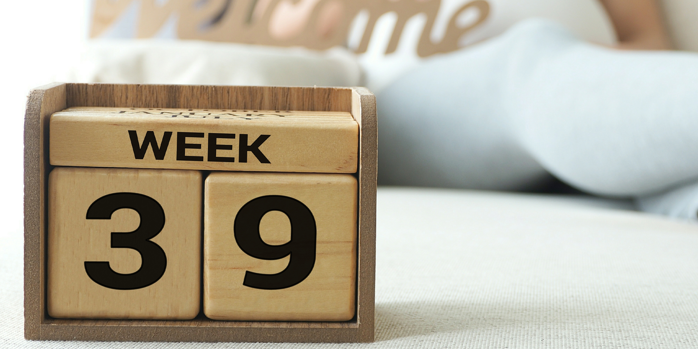 Ein Holzblockkalender zeigt "Woche 39" mit einer schwangeren Frau im Hintergrund, die teilweise unscharf ist | Quelle: Shutterstock