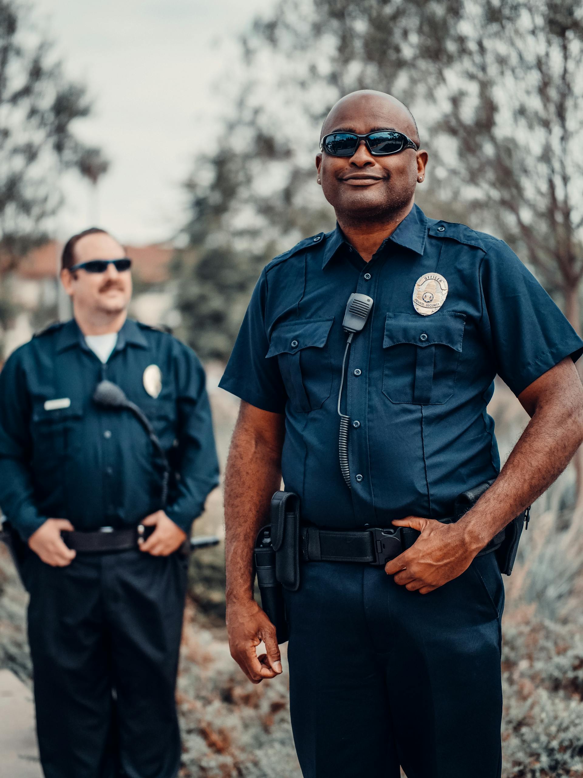 Zwei lächelnde Polizeibeamte in Uniform mit Sonnenbrille | Quelle: Pexels