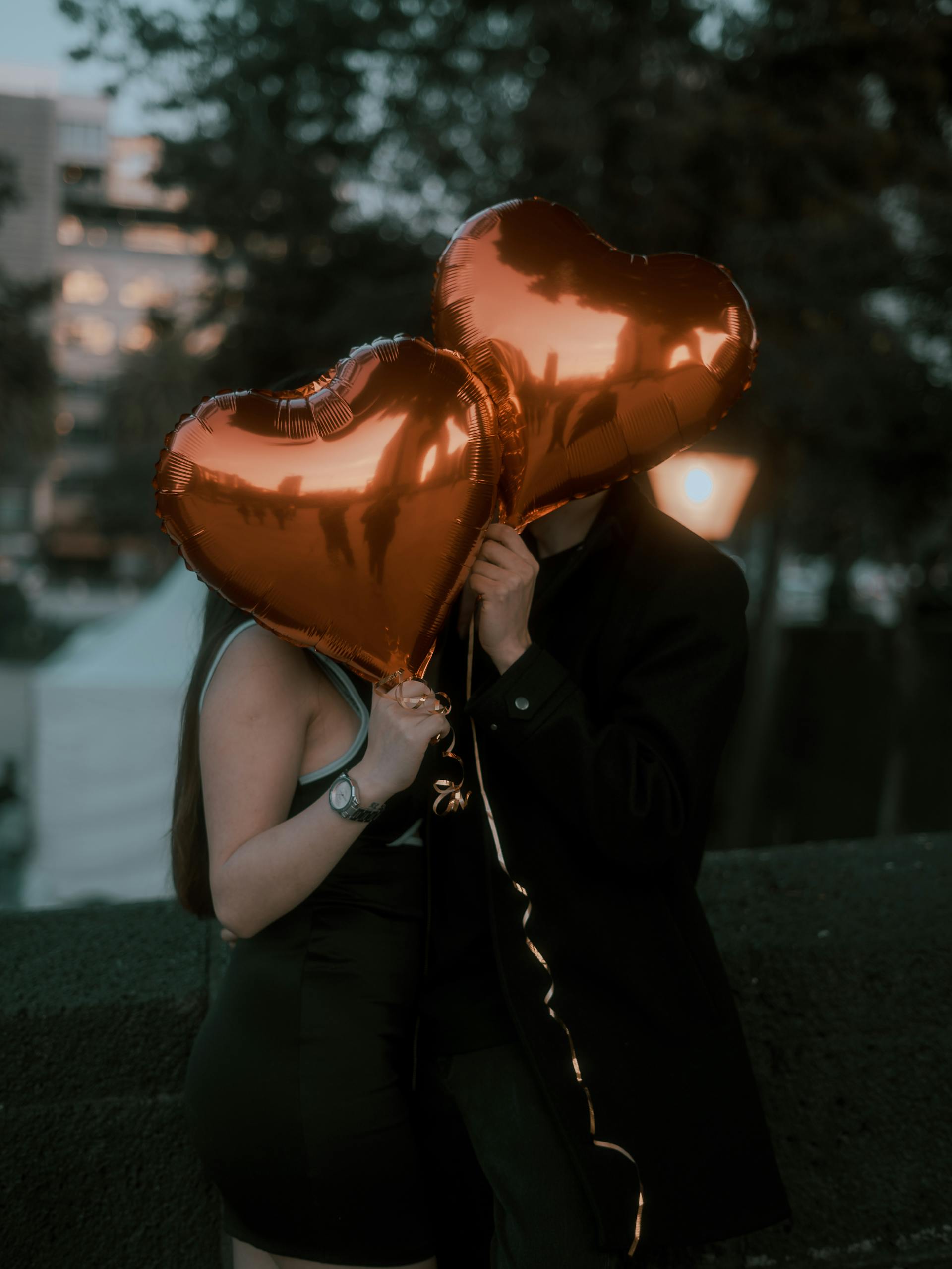 Ein Paar, das seine Gesichter mit herzförmigen Luftballons versteckt | Quelle: Pexels