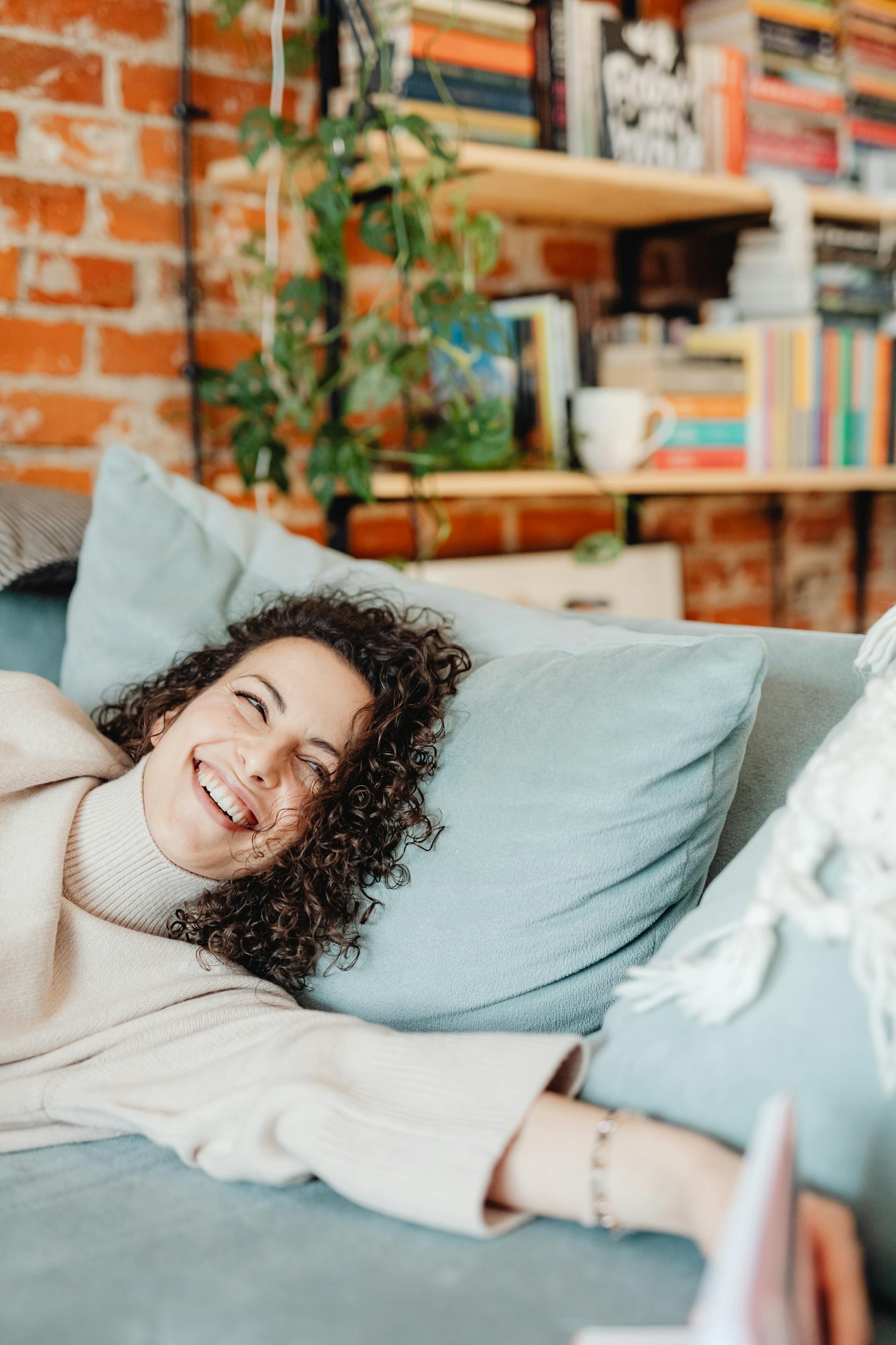 Eine glückliche Frau, die mit einem Lächeln im Gesicht auf einer Couch liegt | Quelle: Pexels