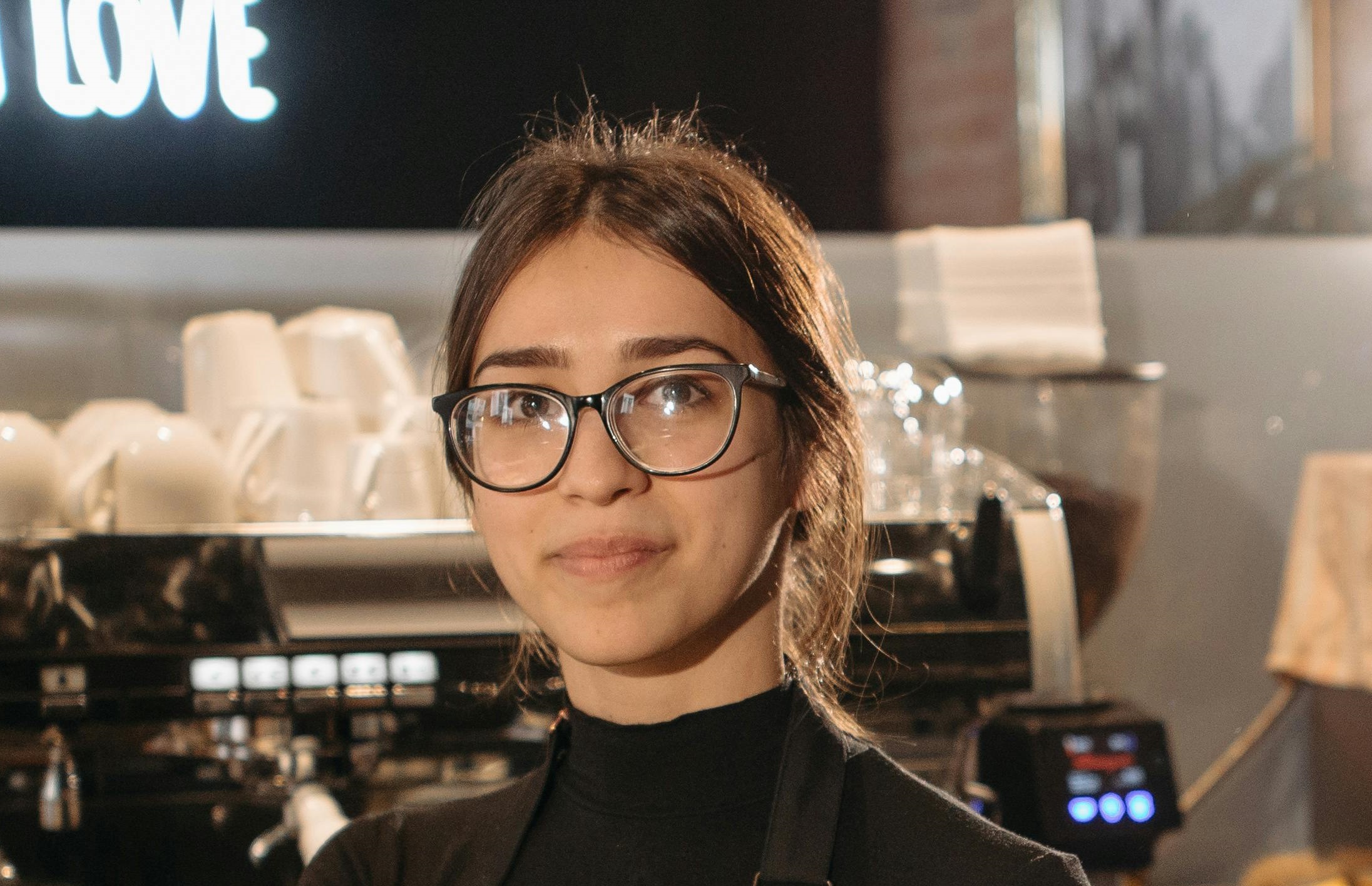 Eine fröhliche Kellnerin mit Brille, die in die Ferne schaut, während sie in einem Café steht | Quelle: Pexels