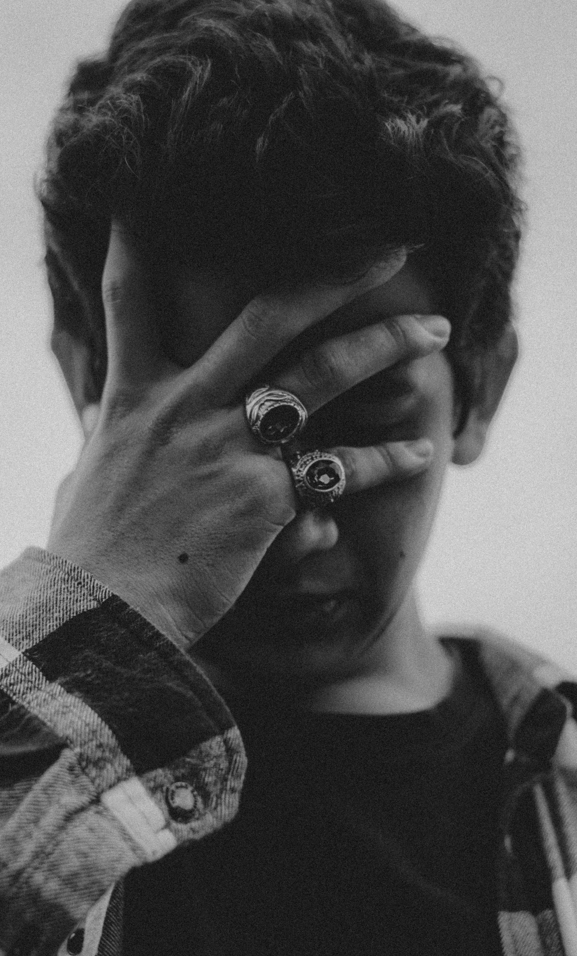Ein Graustufenfoto von einem Jugendlichen, der sein Gesicht verdeckt | Quelle: Pexels