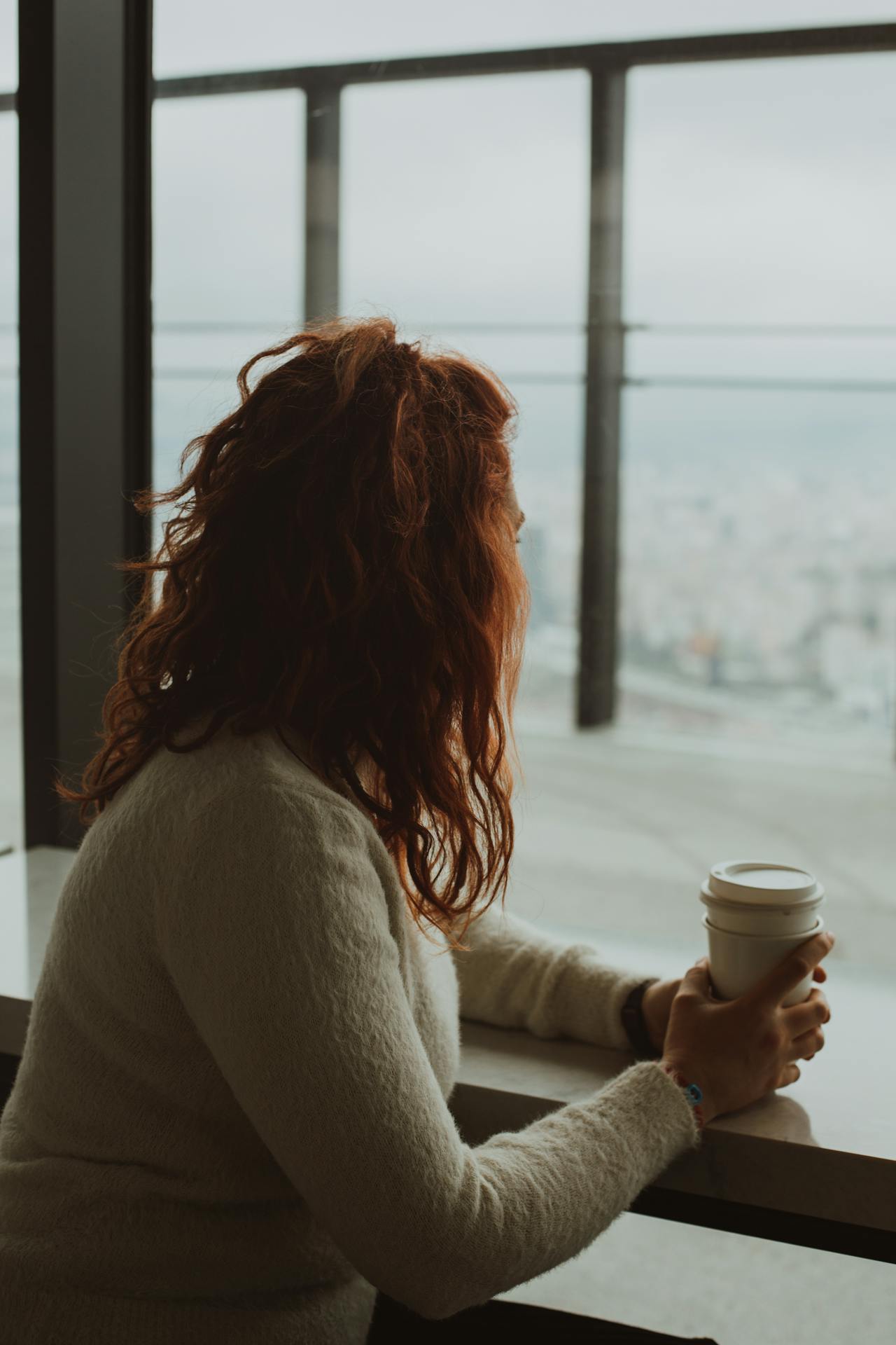 Eine Frau sitzt mit einer Kaffeetasse vor einem Glasfenster | Quelle: Pexels