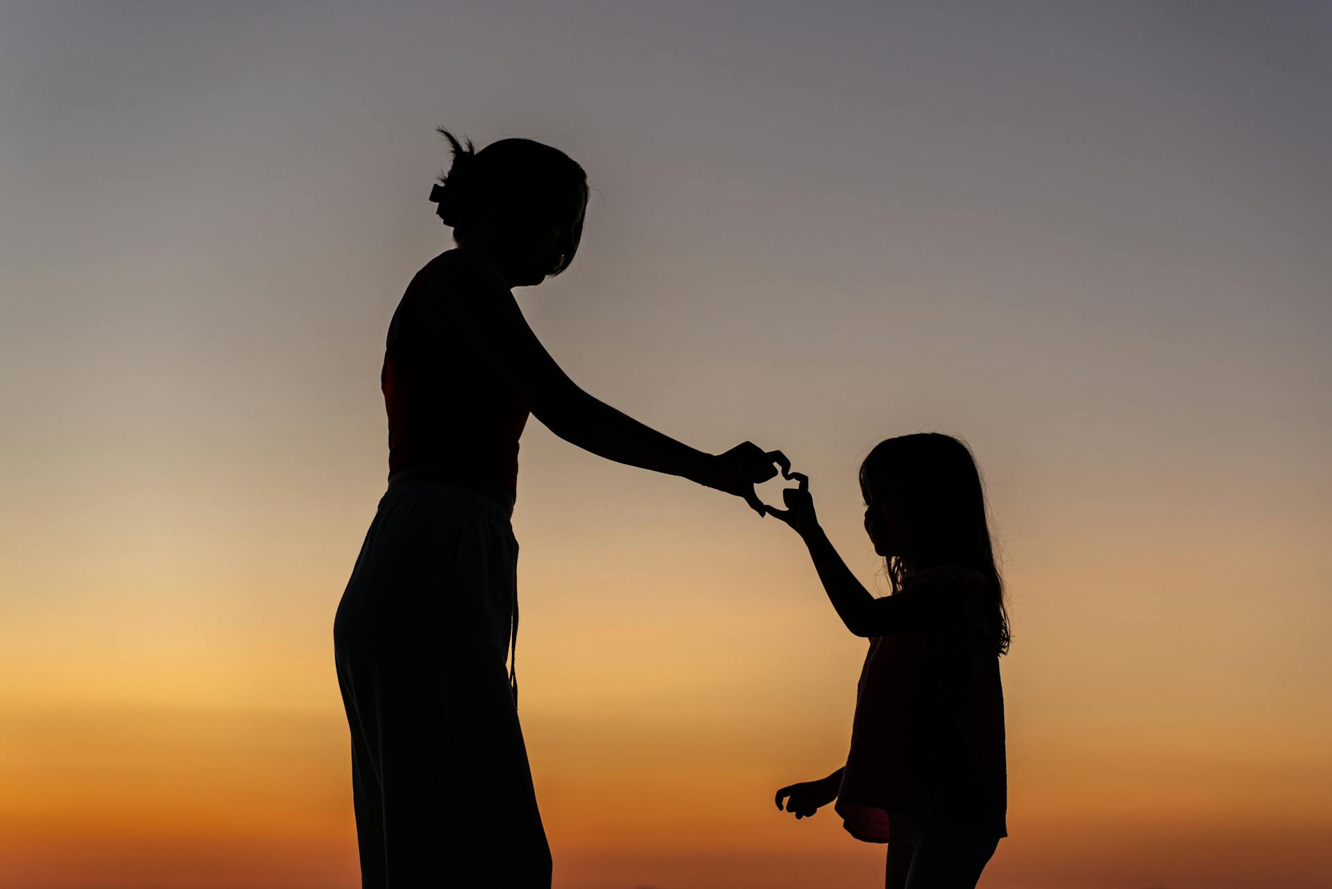 Silhouette einer Mutter und ihrer Tochter, die eine Hand-Herz-Geste machen | Quelle: Pexels