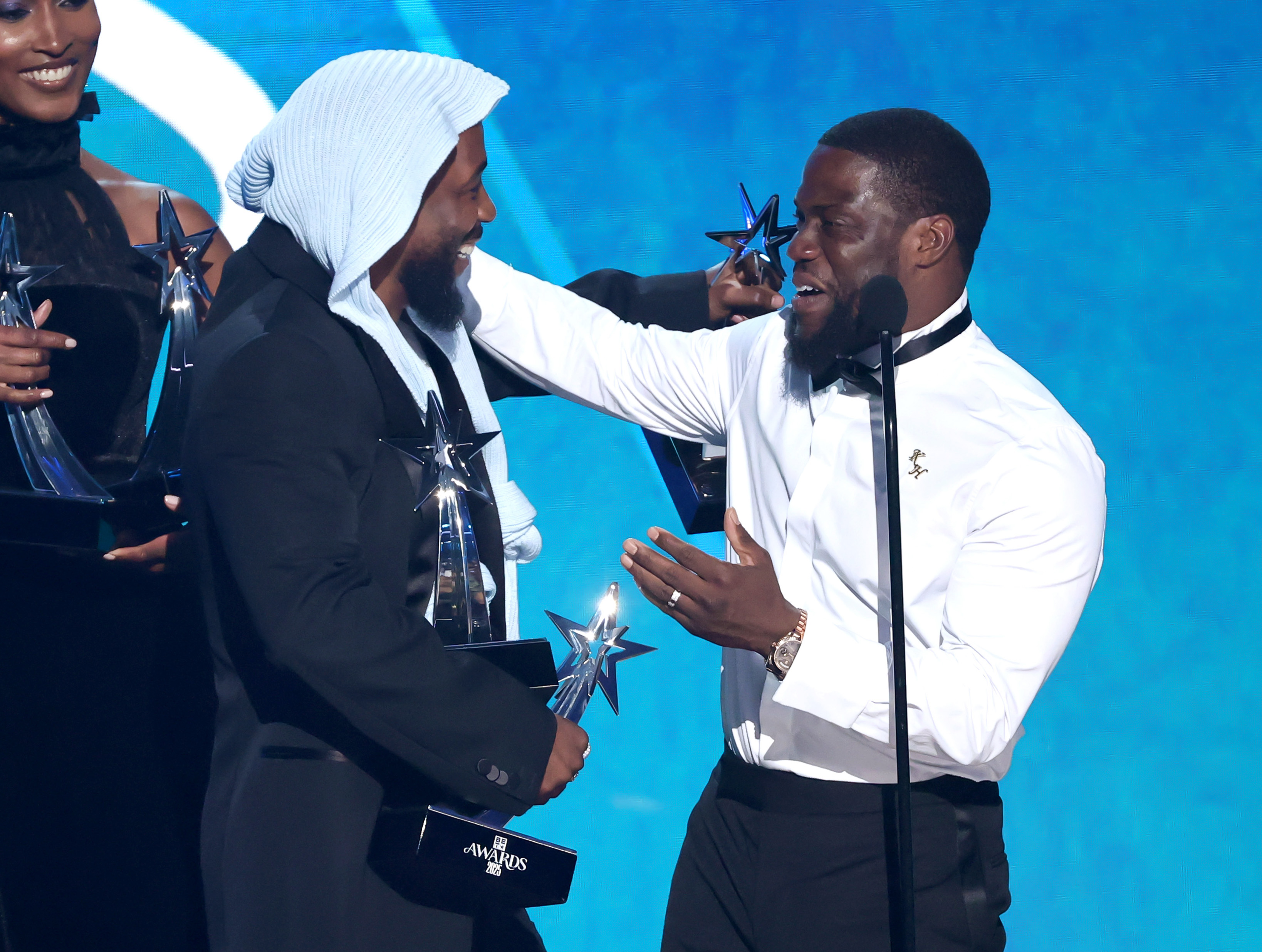 Kevin Hart lacht mit Kendrick Lamar, als er ihm bei den BET Awards 2025 auf der Bühne einen der vielen Preise des Künstlers überreicht. Lamars Hände waren zu diesem Zeitpunkt der Show bereits voller Trophäen.