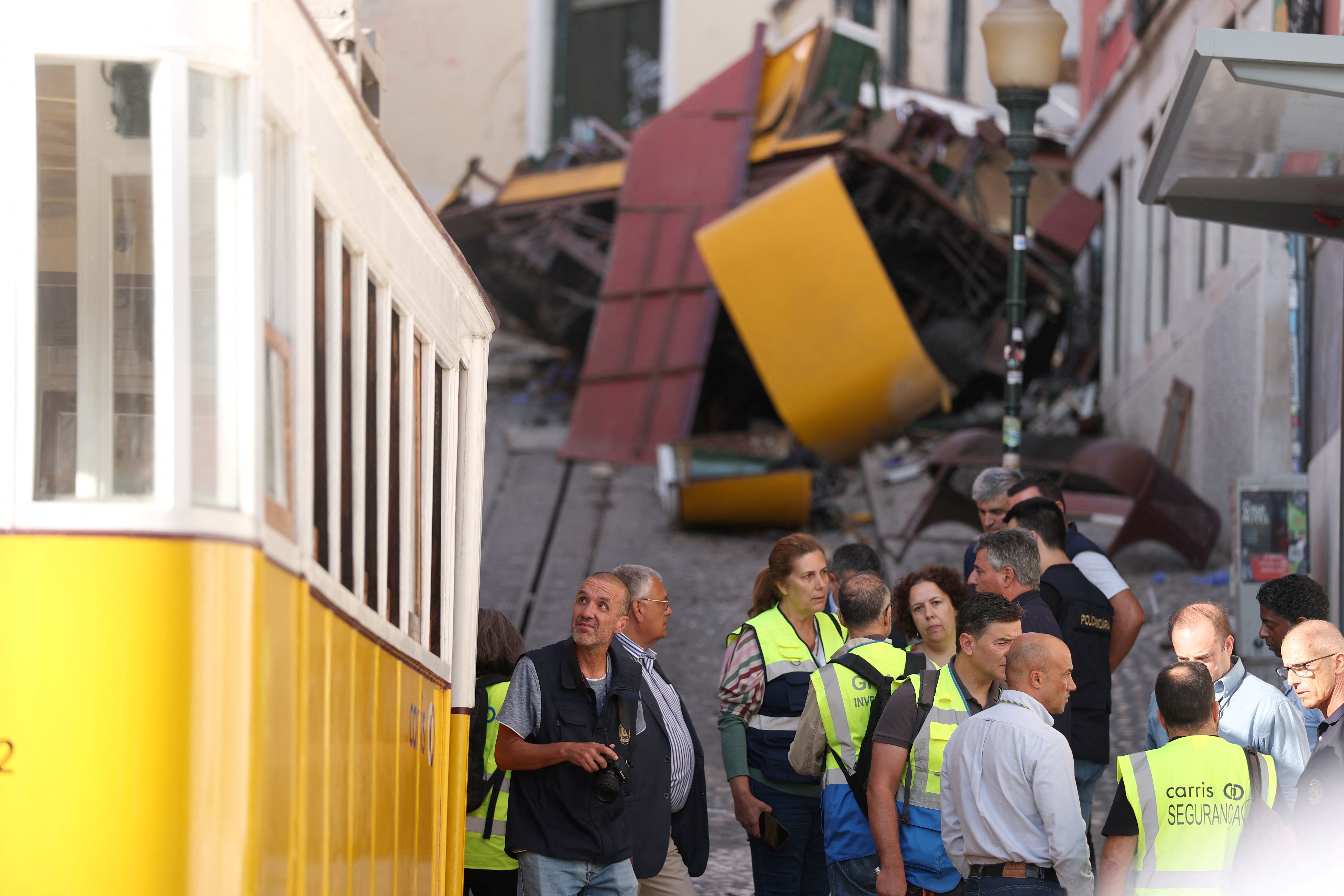 Polizeiermittler (links) neben Mitarbeitern des Lissabonner Verkehrsunternehmens La Carris mit den Trümmern der Gloria-Standseilbahn im Hintergrund einen Tag nach dem Unfall, bei dem am 4. September 2025 in Lissabon 15 Menschen ums Leben kamen | Quelle: Getty Images