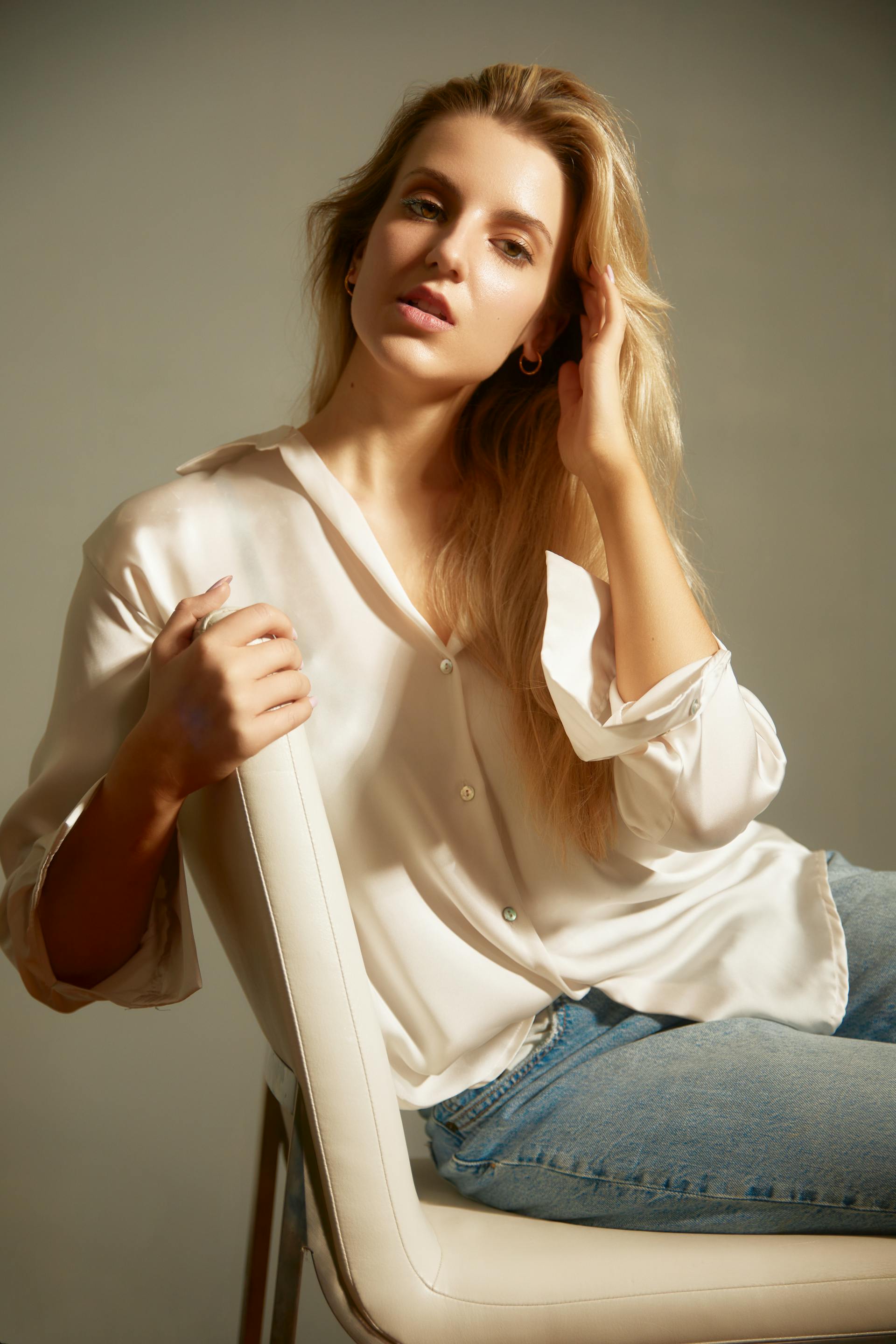 Eine blonde Frau in einem weißen Seidenhemd und Jeans sitzt auf einem weißen Stuhl | Quelle: Pexels