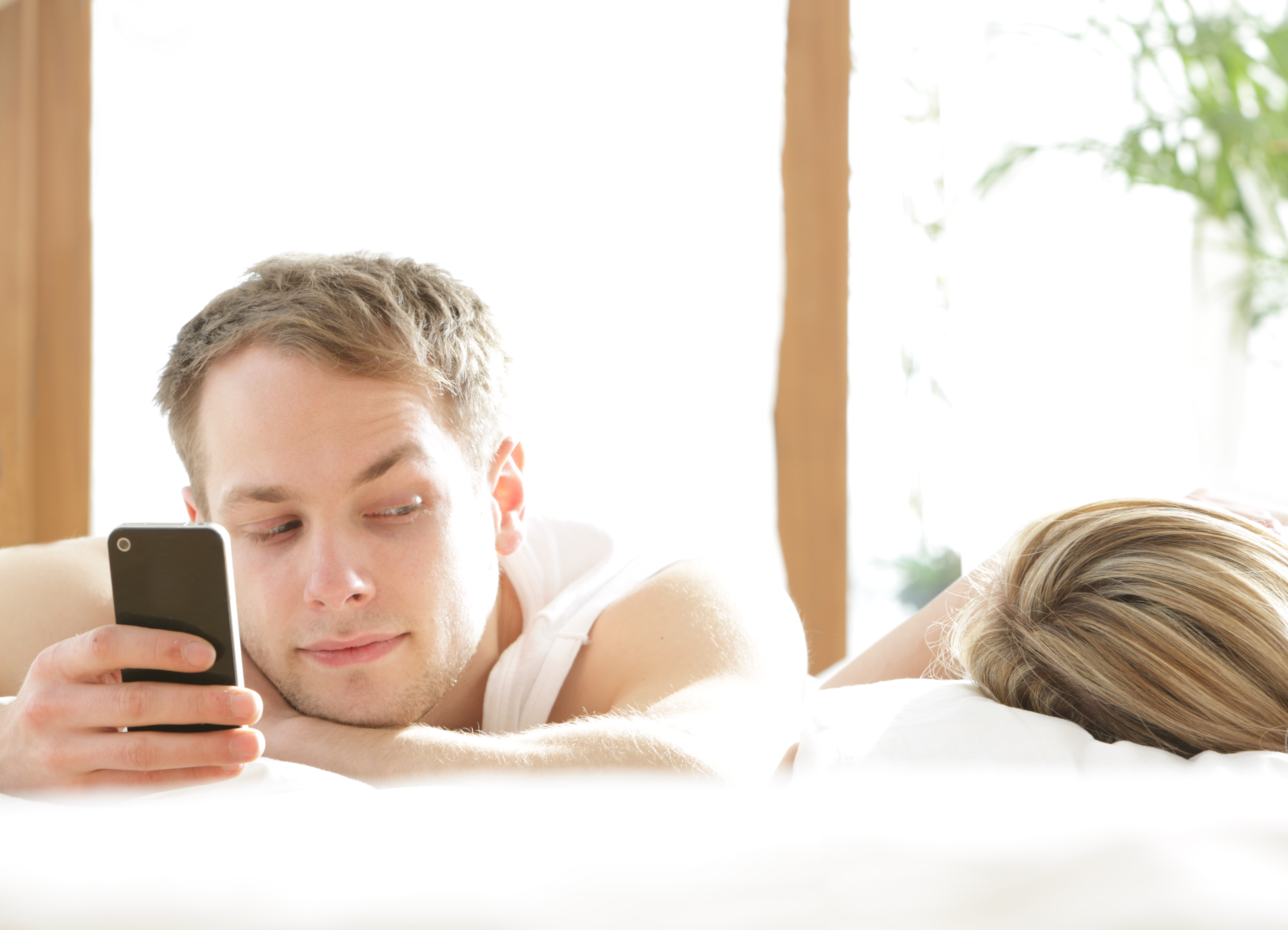 Mann mit Telefon im Bett, schaut auf eine schlafende Frau | Quelle: Getty Images