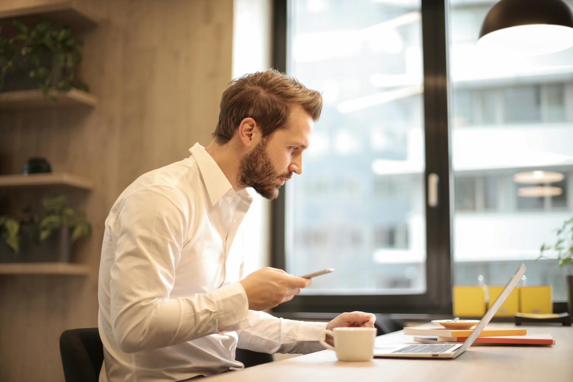 Ein Mann arbeitet an seinem Schreibtisch mit einem Laptop und einem Handy | Quelle: Pexels