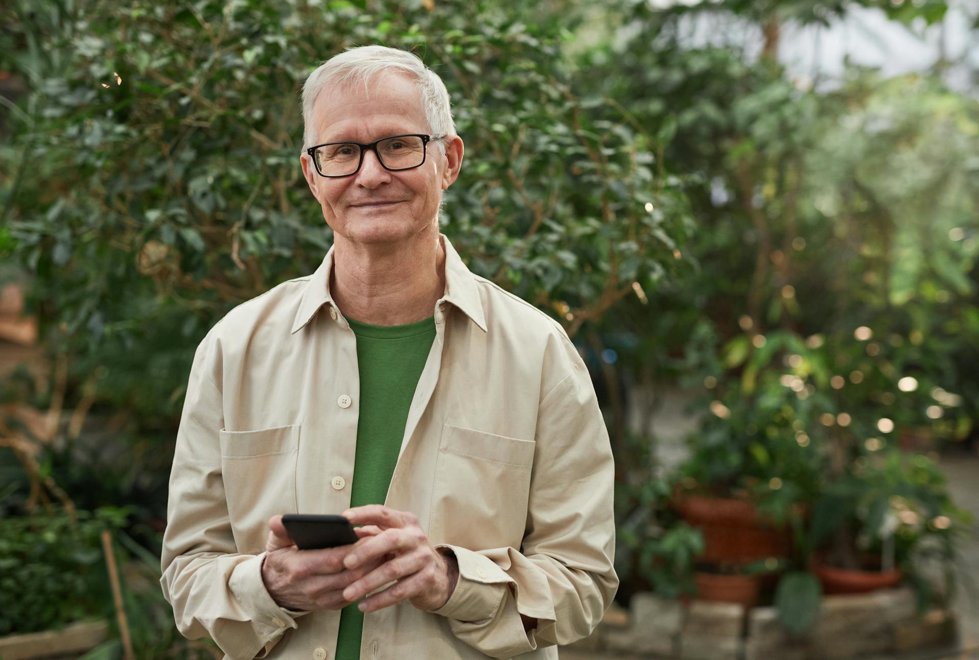 Ein glücklicher reifer Mann mit Brille und Button-up-Hemd, der ein Telefon hält | Quelle: Pexels