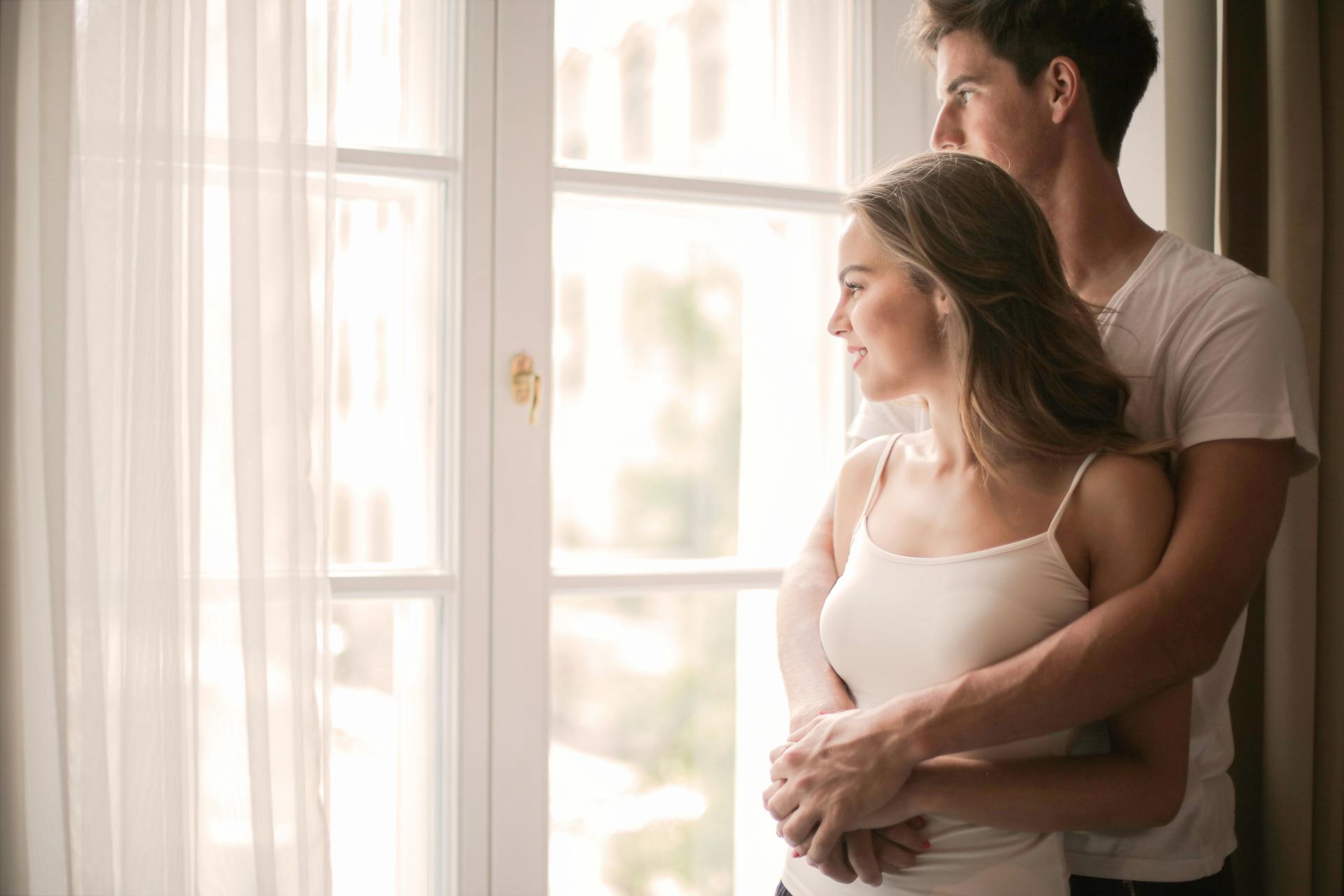 Ein kuschelndes Pärchen in der Nähe des Fensters in einem Zimmer | Quelle: Pexels