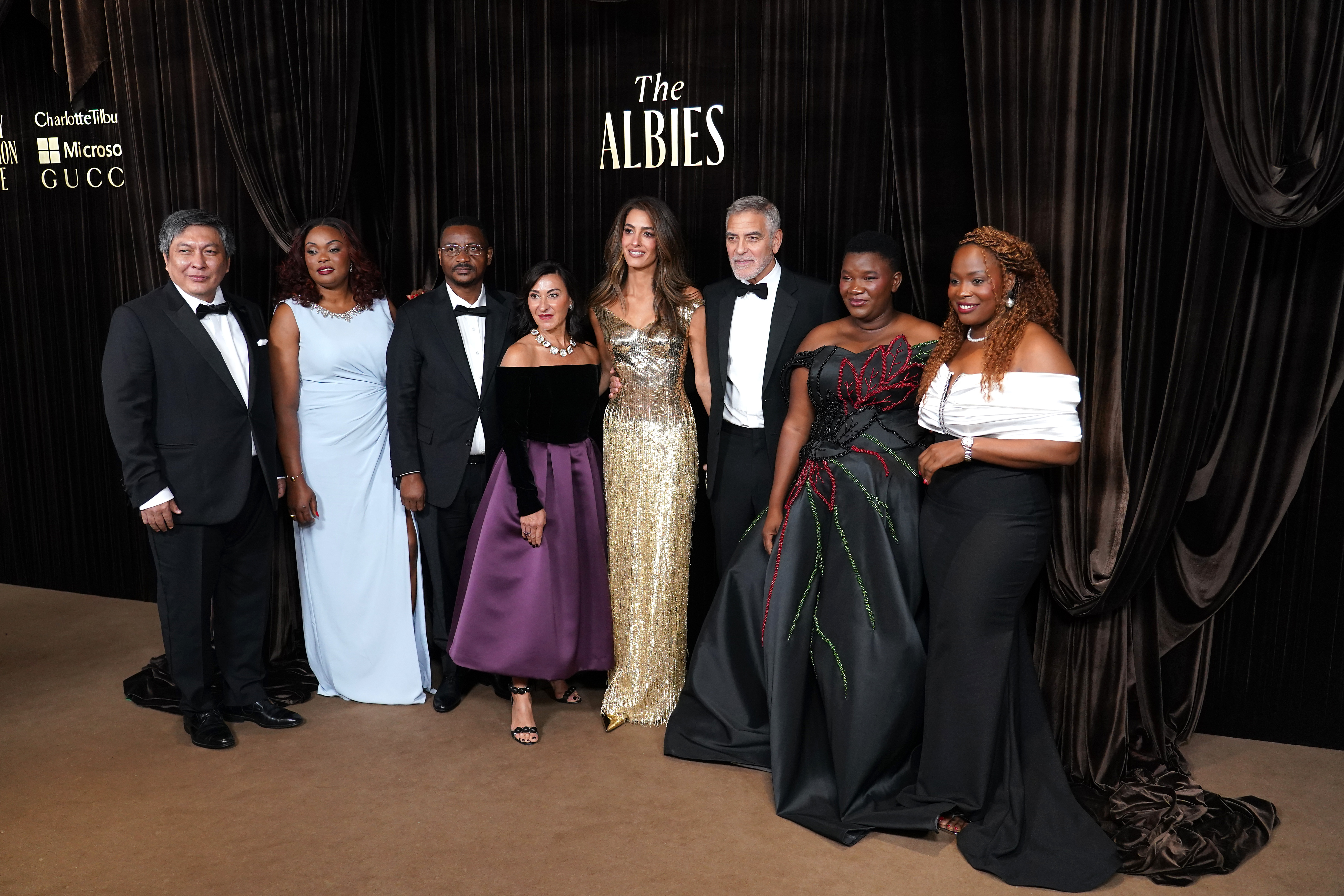 George Clooney und Amal Clooney posieren am 9. Oktober im Londoner Naturkundemuseum mit anderen Gästen und Preisträgern bei den „Albies 2026“ der Clooney Foundation for Justice. Die Gruppe steht vor einem mit schwarzen Vorhängen versehenen Hintergrund mit dem „The Albies“-Logo, gekleidet in festlicher Abendgarderobe, wobei einige Gäste ihre bodenlangen Abendkleider zur Schau stellen. | Quelle: Getty Images