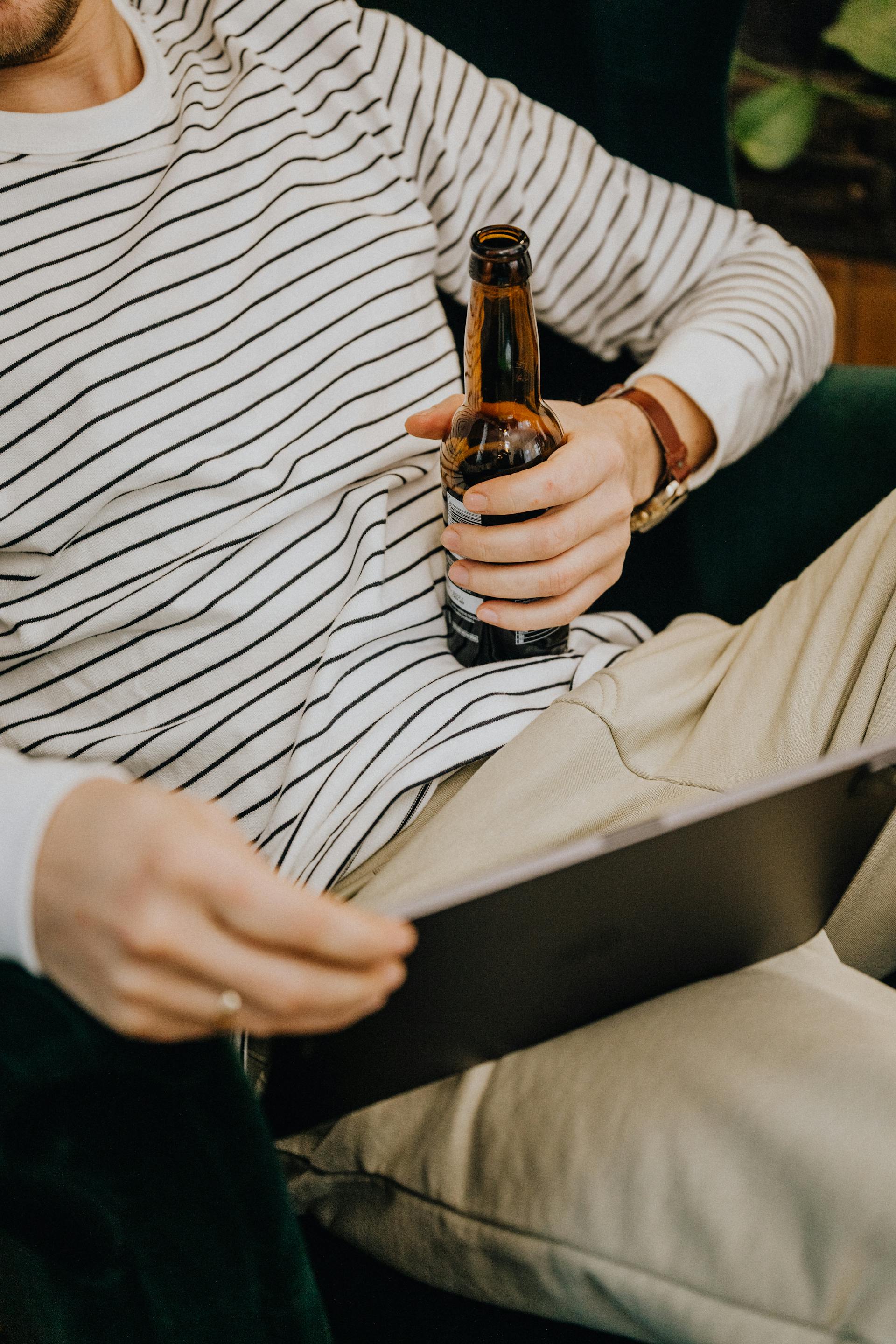 Nahaufnahme eines Mannes, der eine Bierflasche in der Hand hält und auf sein Tablet schaut | Quelle: Pexels