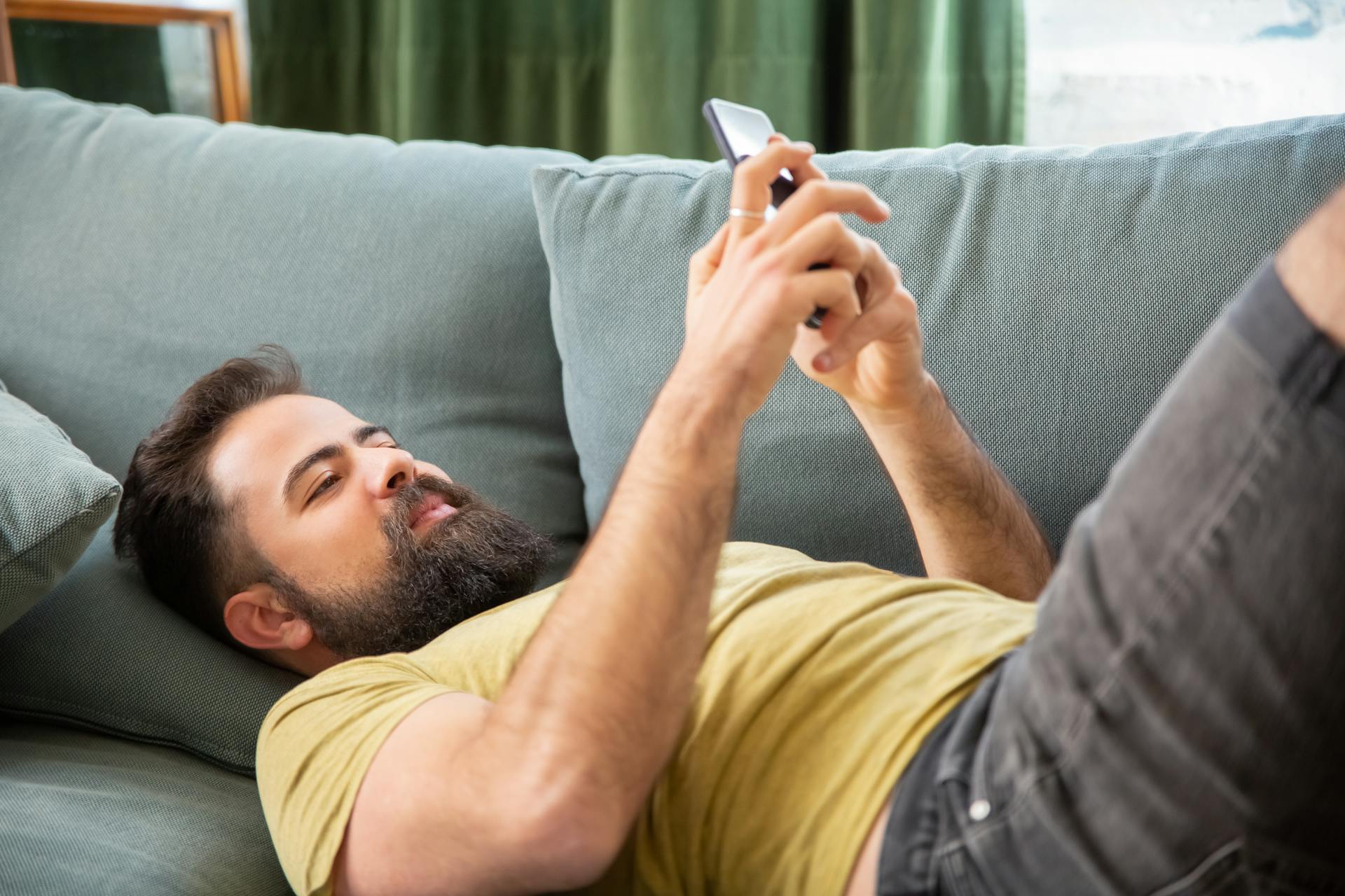 Ein Mann benutzt sein Telefon, während er auf dem Sofa liegt | Quelle: Pexels