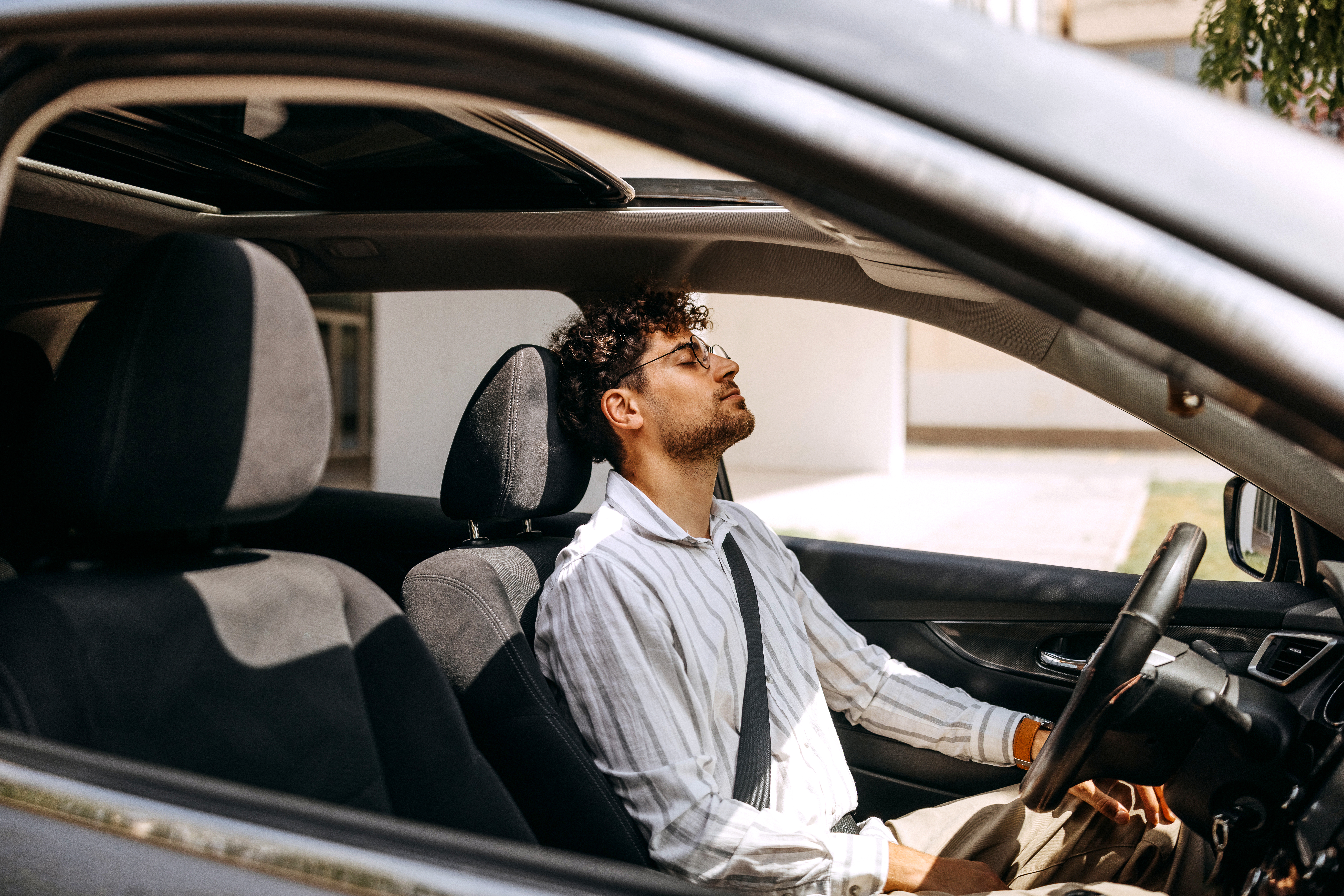Müder junger gut gekleideter Mann sitzt im Auto | Quelle: Getty Images