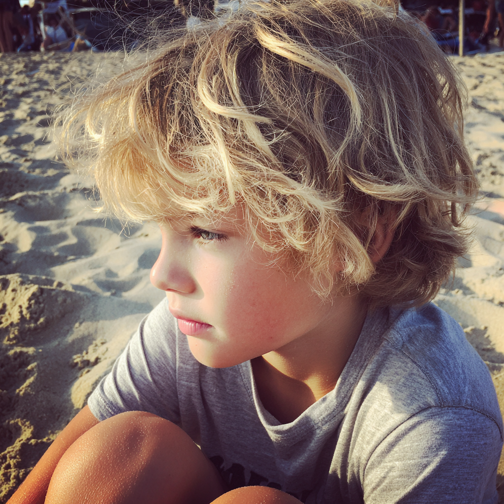 Ein kleiner Junge sitzt am Strand | Quelle: Midjourney