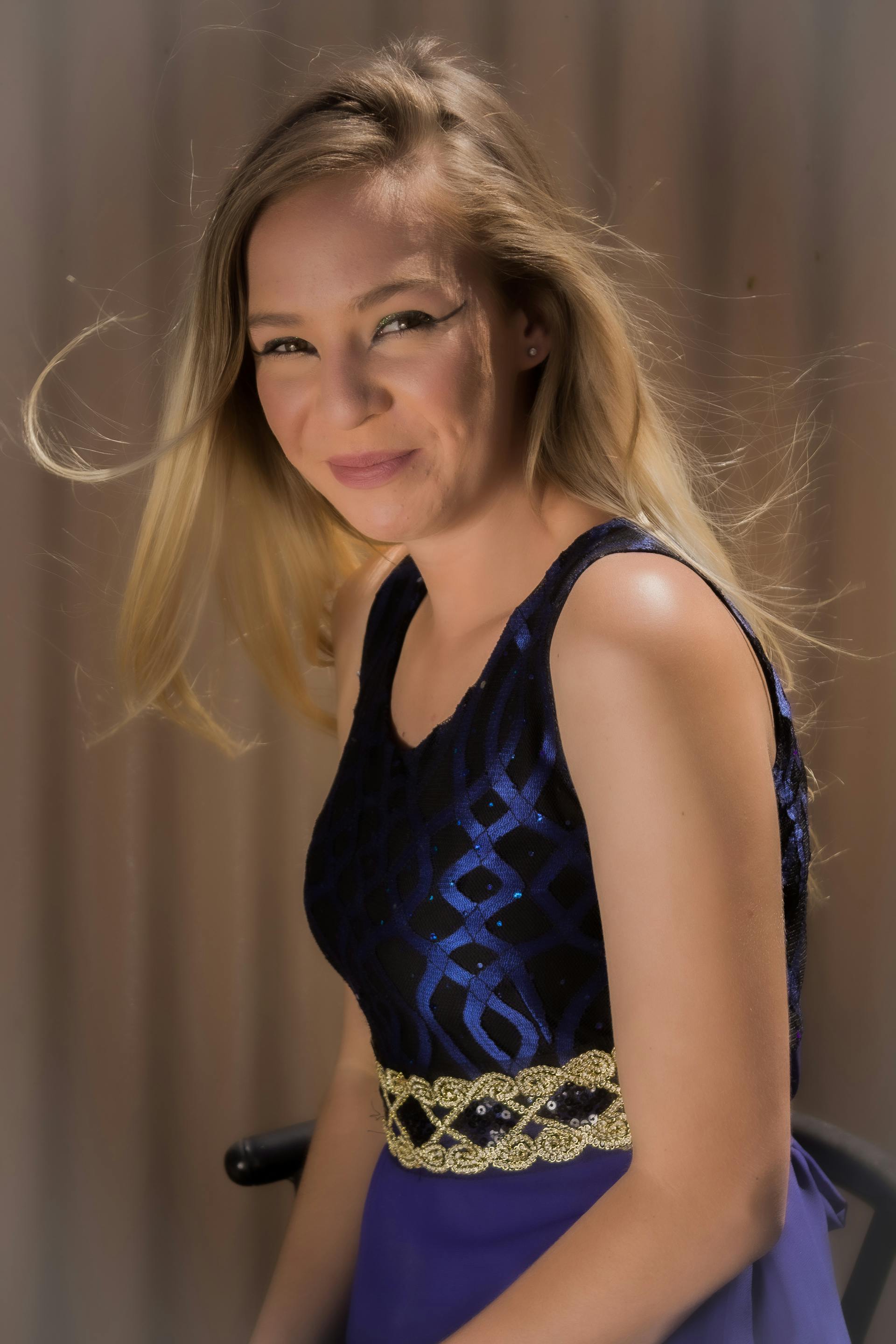 Eine schöne junge Frau mit blonden Haaren, die lächelt und ein glitzerndes blau-goldenes Kleid trägt | Quelle: Pexels