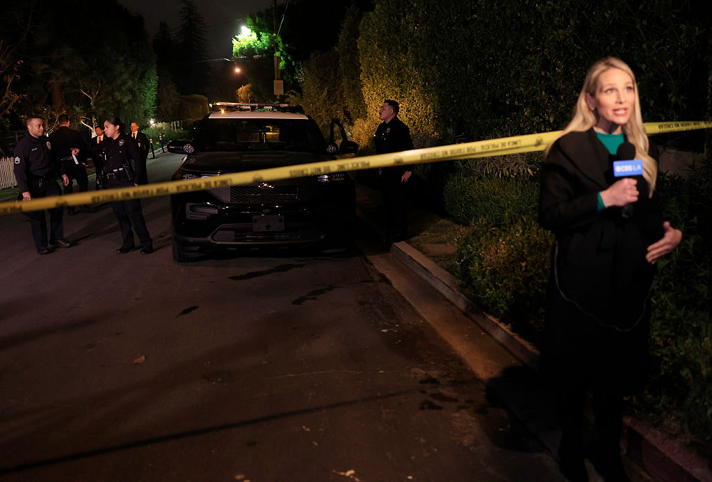 Ein Reporter arbeitet in der Nähe von LAPD-Beamten, die Wache stehen, während die Polizei zwei Personen untersucht, die am 14. Dezember 2025 in Rob Reiners Haus in Brentwood, Kalifornien, tot aufgefunden wurden. | Quelle: Getty Images