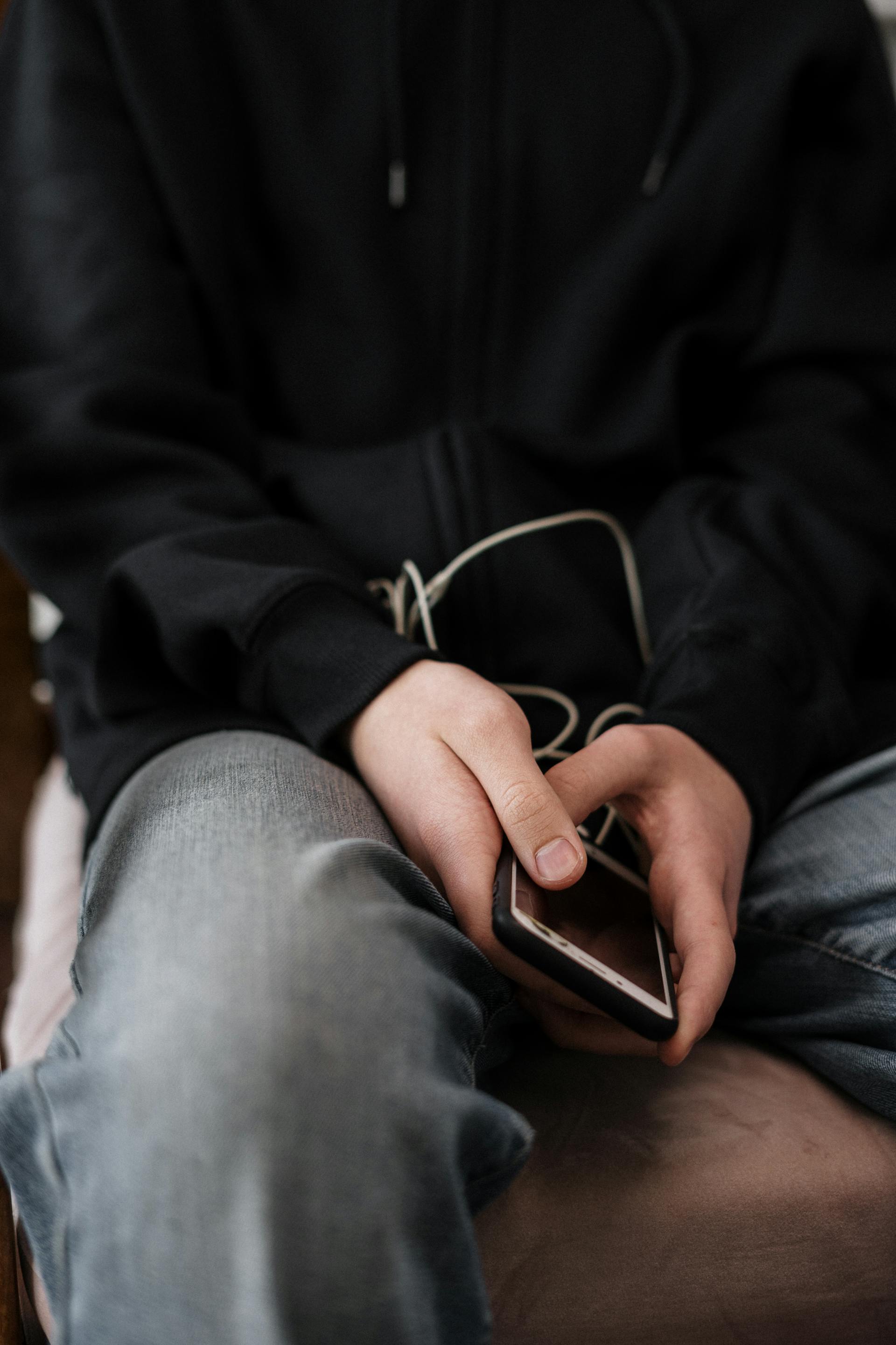 Eine Nahaufnahme einer Person in Jacke und Jeans, die ein Telefon hält | Quelle: Pexels