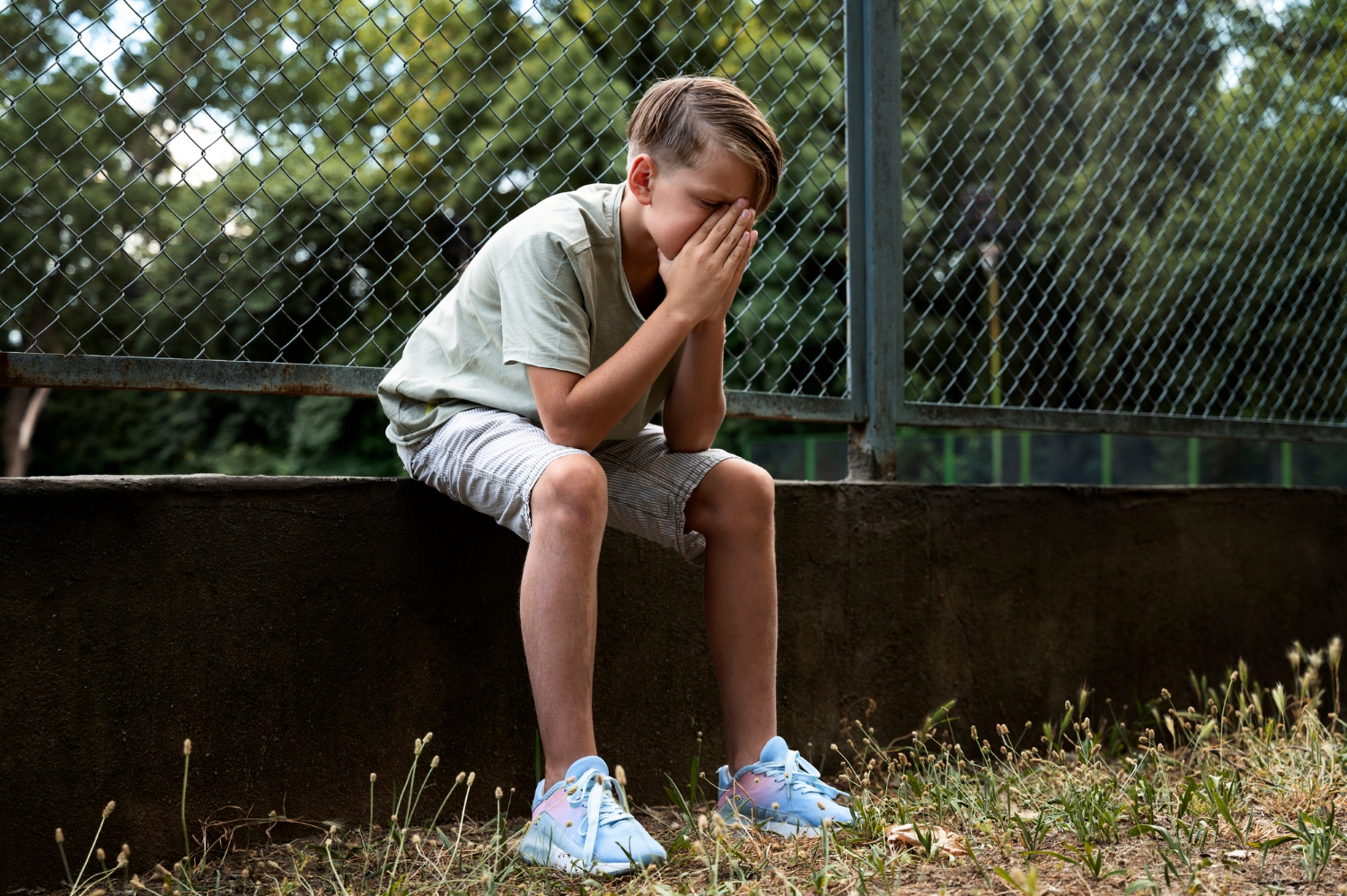 Ein Junge mit gebrochenem Herzen sitzt auf einer niedrigen Zaunmauer | Quelle: Freepik