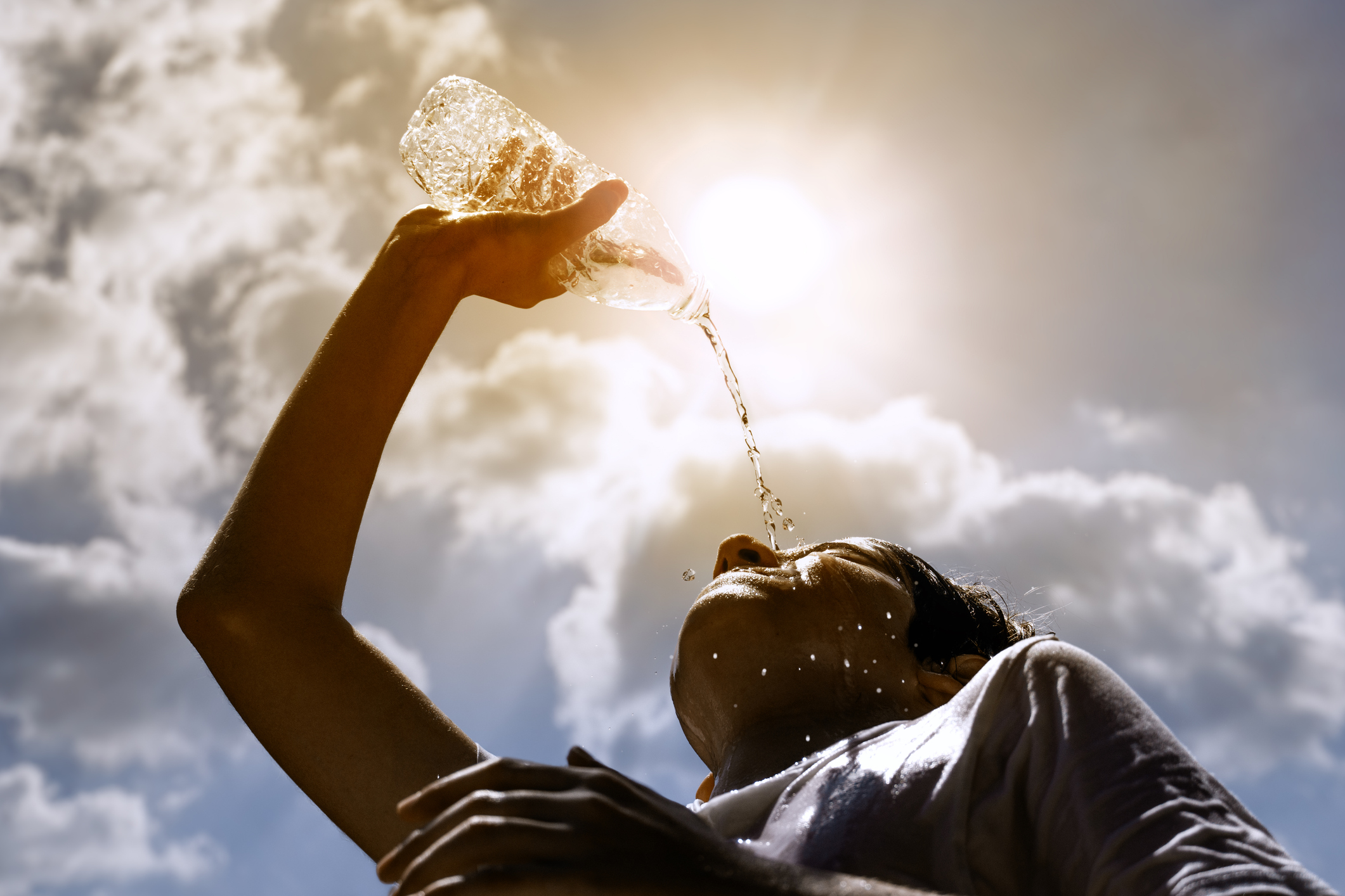 Junge Frau, die unter der heißen Sommersonne frisches Wasser aus einer Plastikflasche trinkt | Quelle: Getty Images