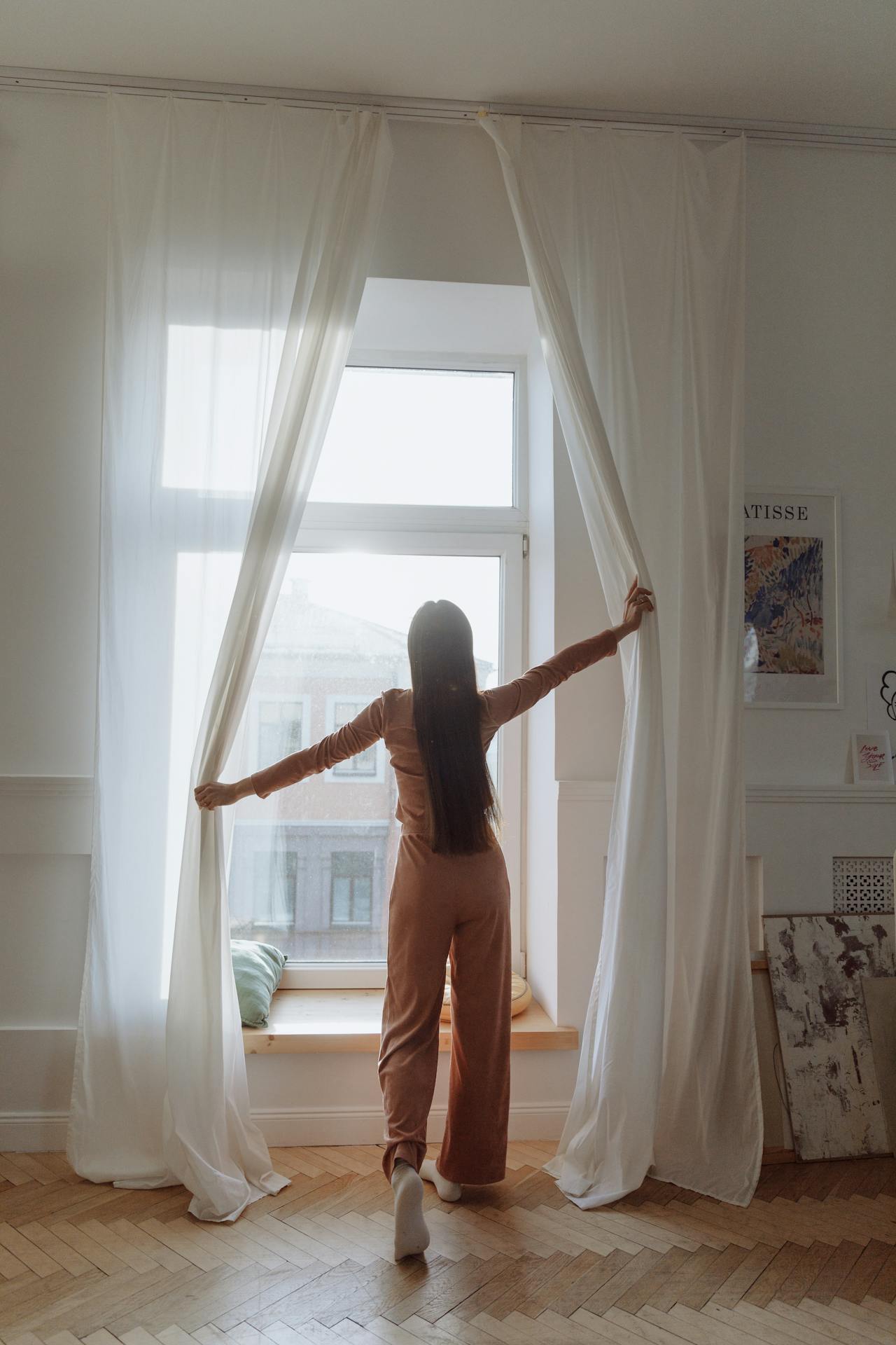 Eine Frau steht am Fenster und öffnet die Vorhänge | Quelle: Pexels