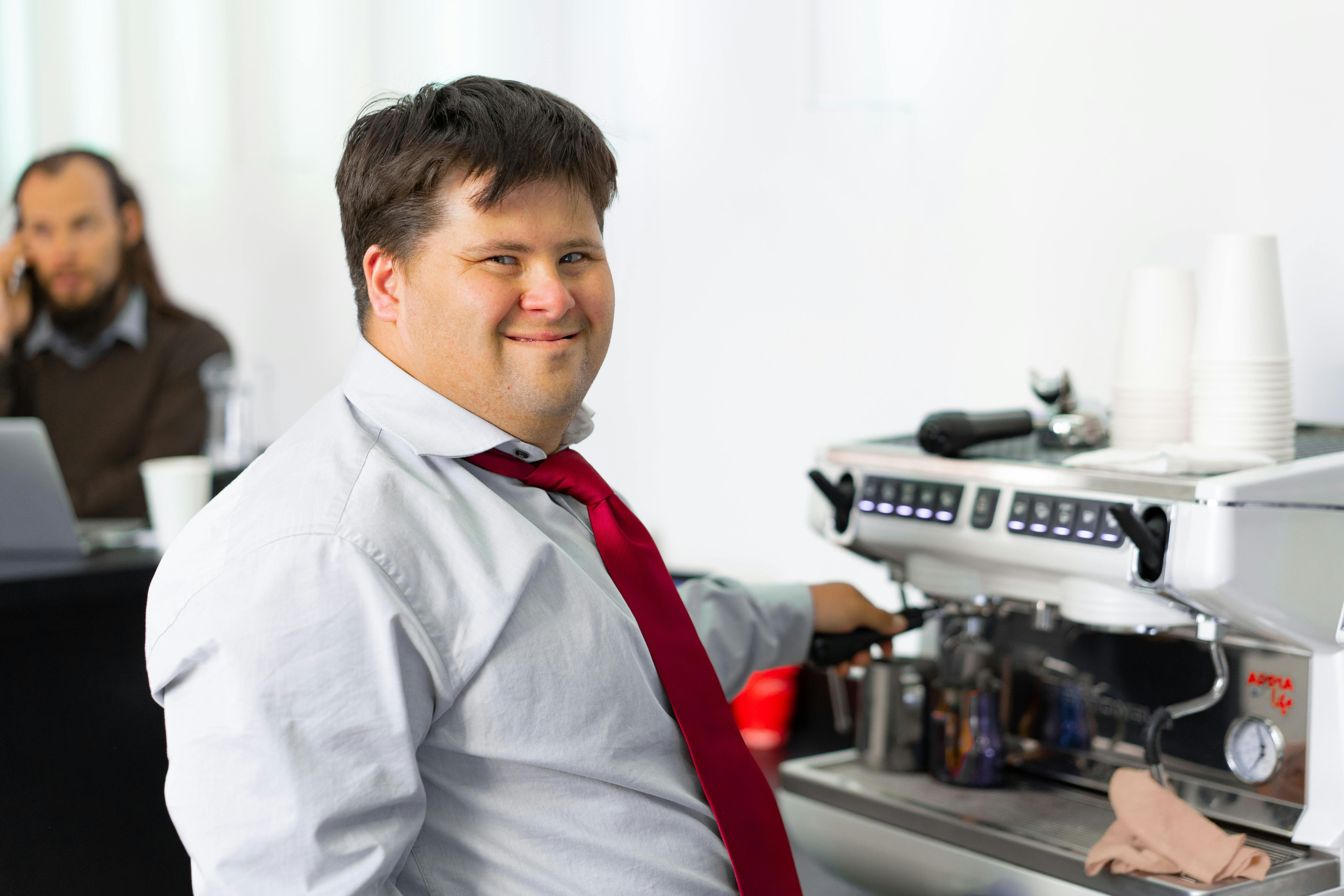 Ein Mann lächelt, während er an einer Kaffeemaschine steht | Quelle: Pexels