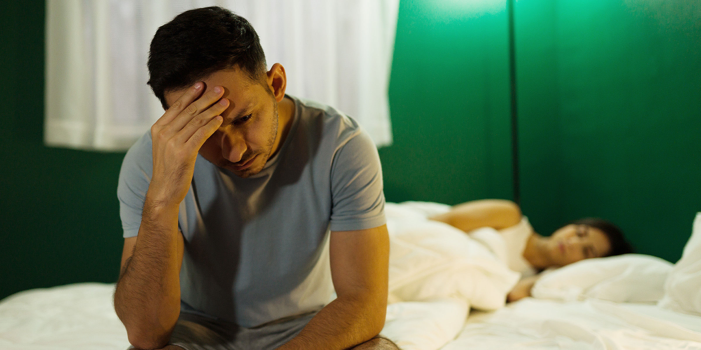 Ein gestresster Ehemann sitzt auf einem Bett, während seine Frau schläft | Quelle: Shutterstock