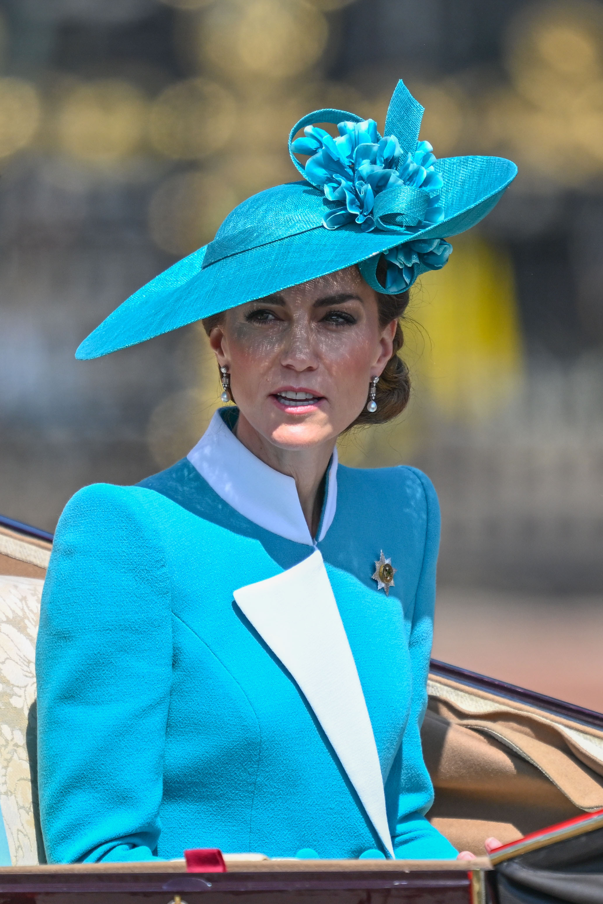 Auf dieser mittelgroßen Aufnahme sieht man Prinzessin Catherine in ihrem türkisfarbenen und weißen Ensemble während des Trooping the Colour 2025. Das Design ihres strukturierten Blazers ist deutlich zu erkennen, mit kräftigen weißen Akzenten am Kragen und an den Manschetten, die einen Kontrast zu dem sattgrünen Stoff bilden. Mit ihrer Haltung und Gelassenheit verkörpert sie moderne königliche Eleganz.