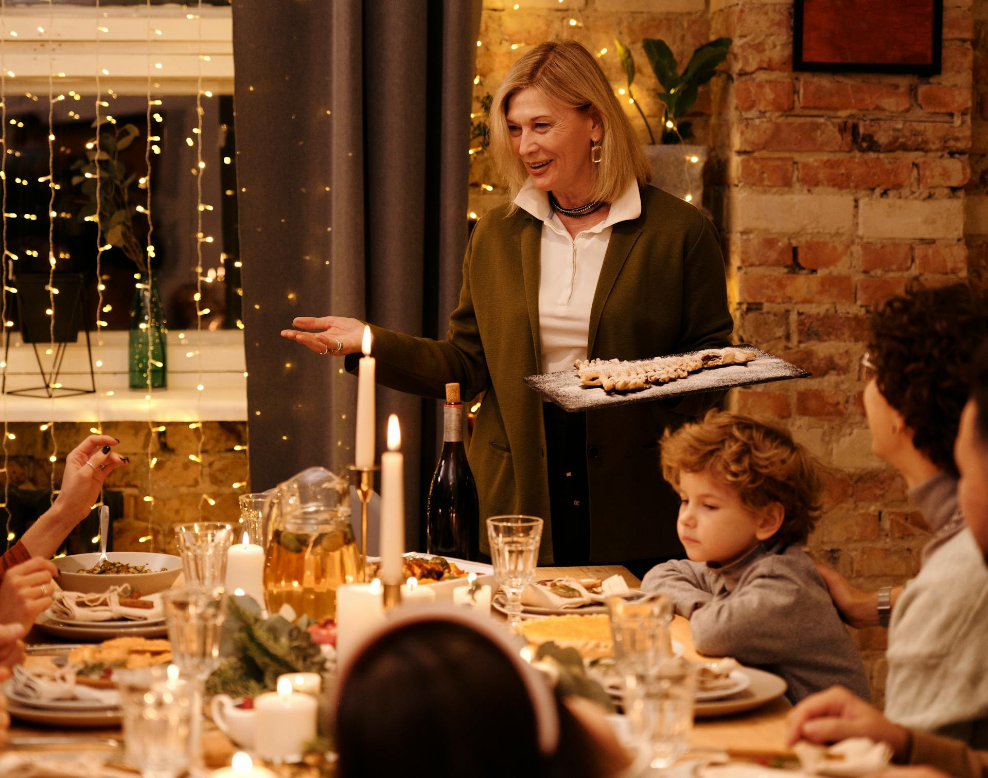 Eine Frau serviert ihrer Familie das Essen an einem Esstisch mit Kerzen und Lichterketten | Quelle: Pexels