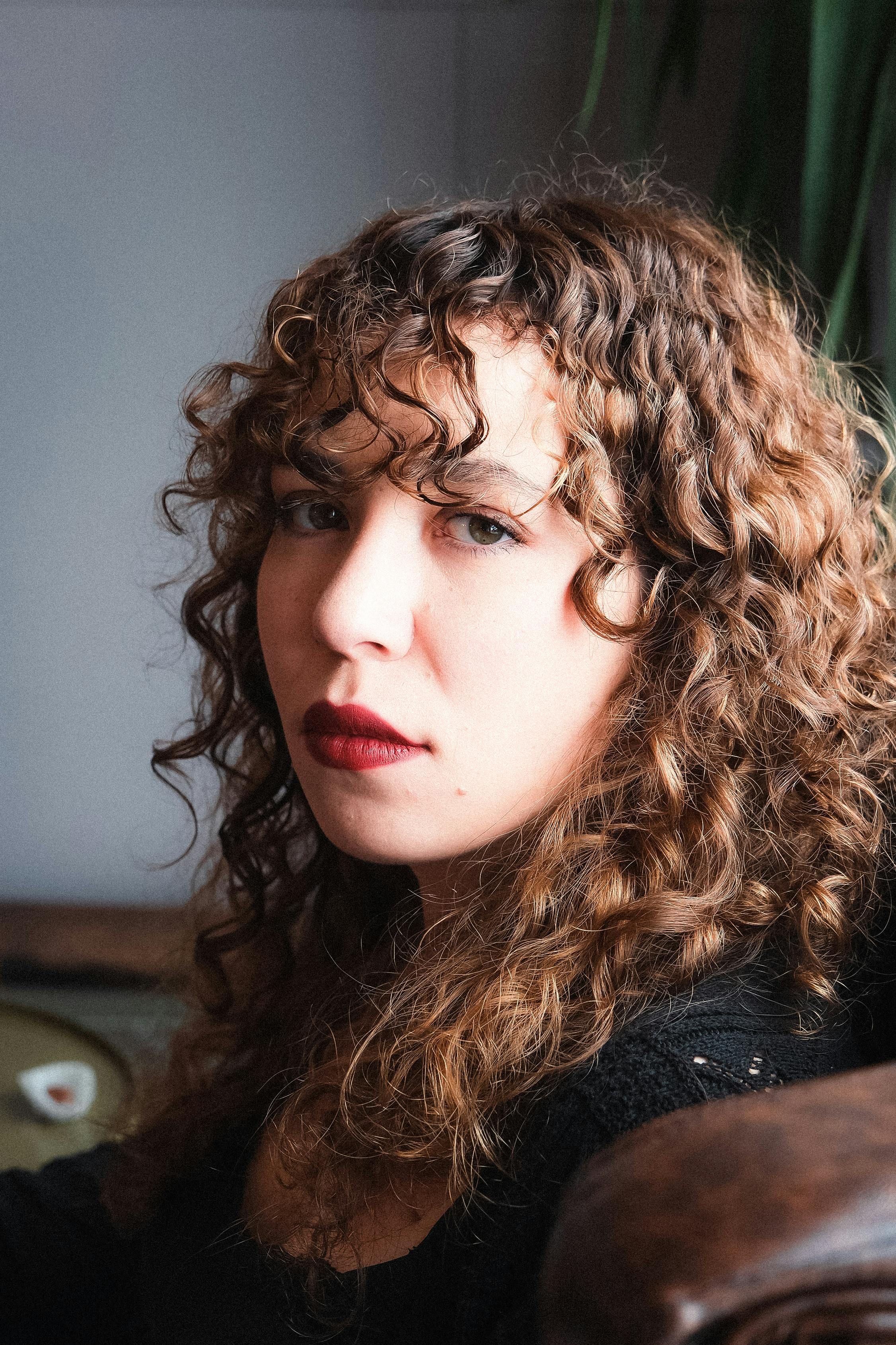 Eine nachdenkliche Frau mit lockigem Haar und rotem Lippenstift | Quelle: Pexels