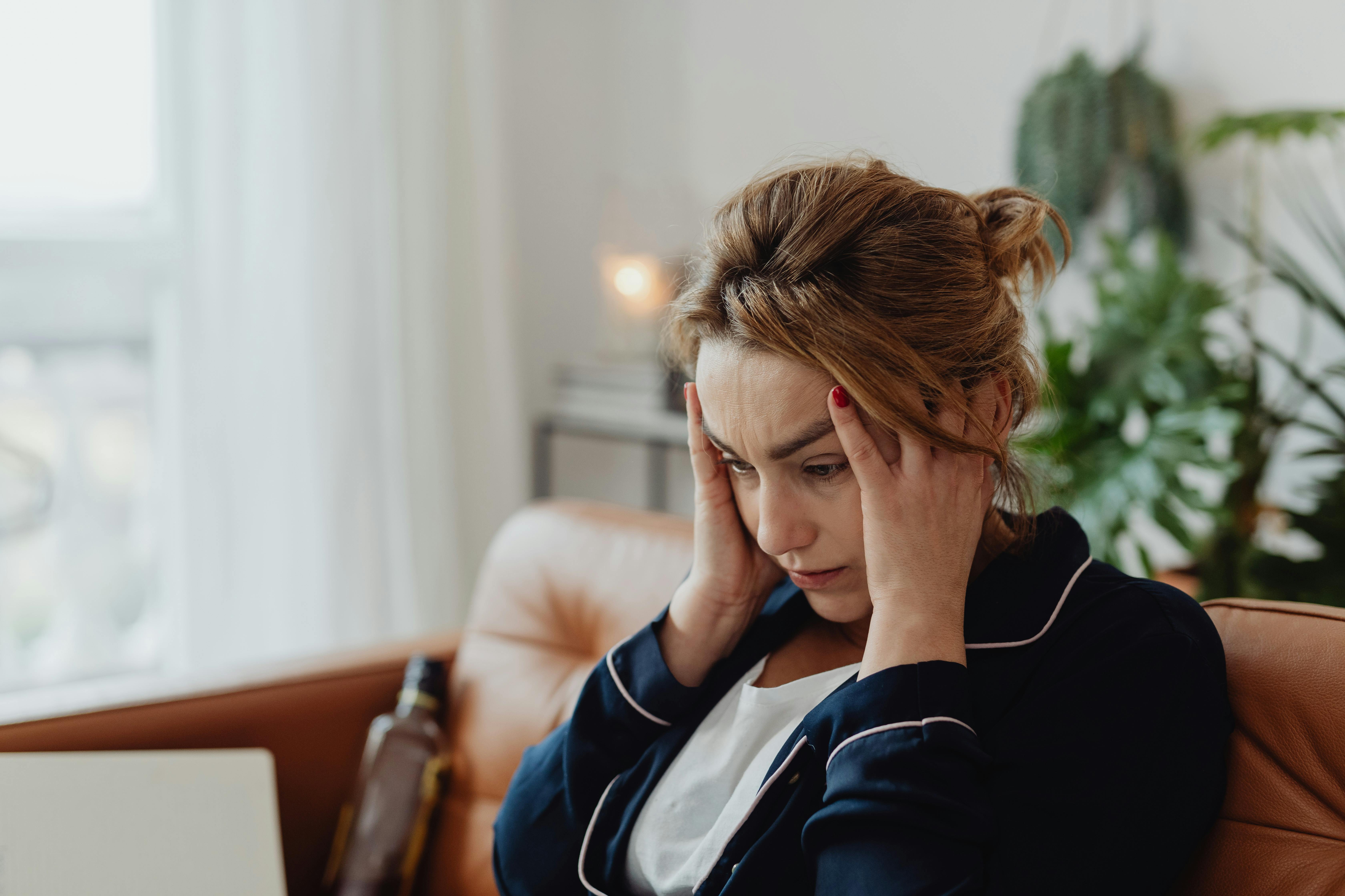 Eine Frau, die auf einer Couch sitzt und sich den Kopf hält | Quelle: Pexels