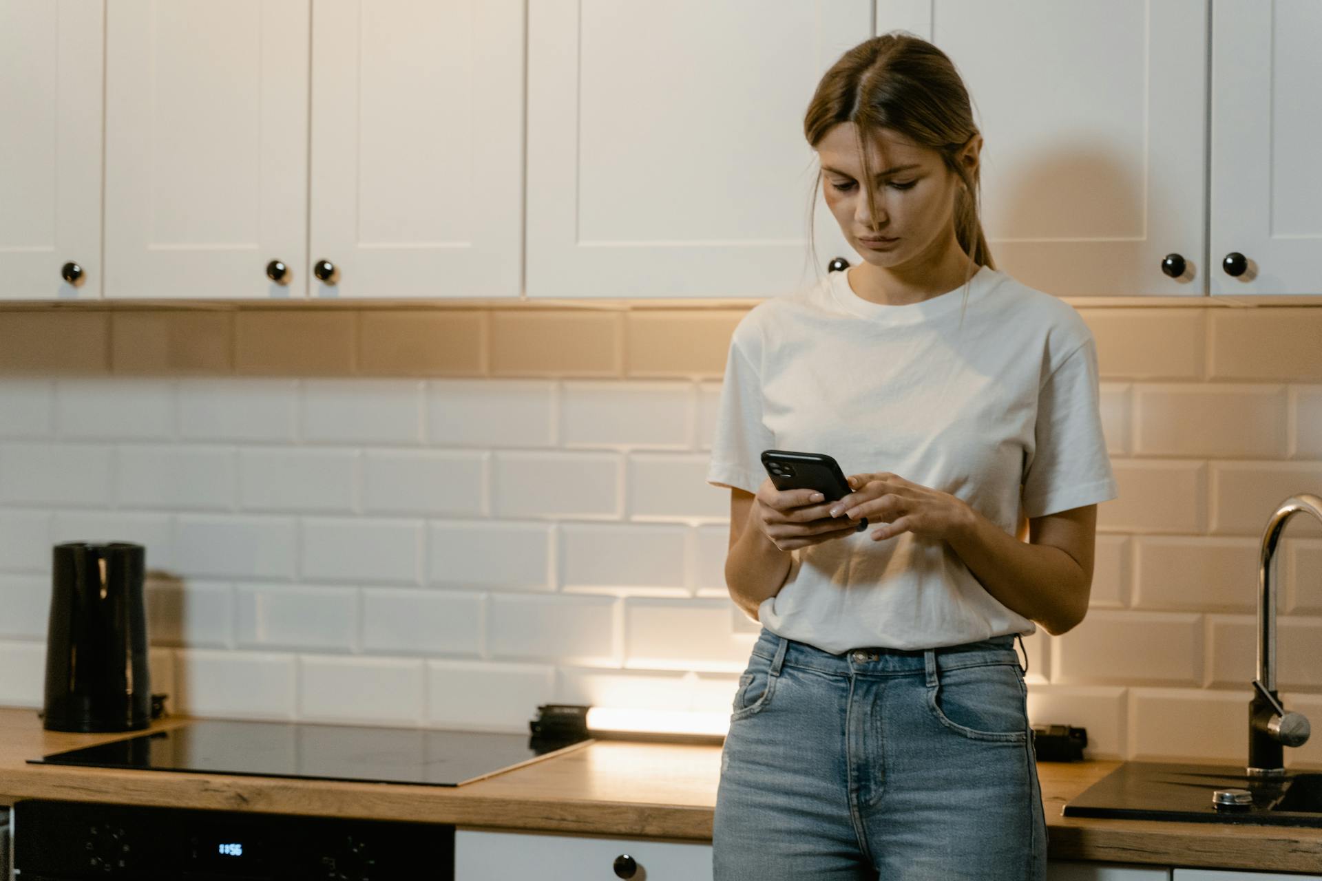 Eine Frau in weißem T-Shirt und Jeans telefoniert, während sie in einer Küche steht | Quelle: Pexels