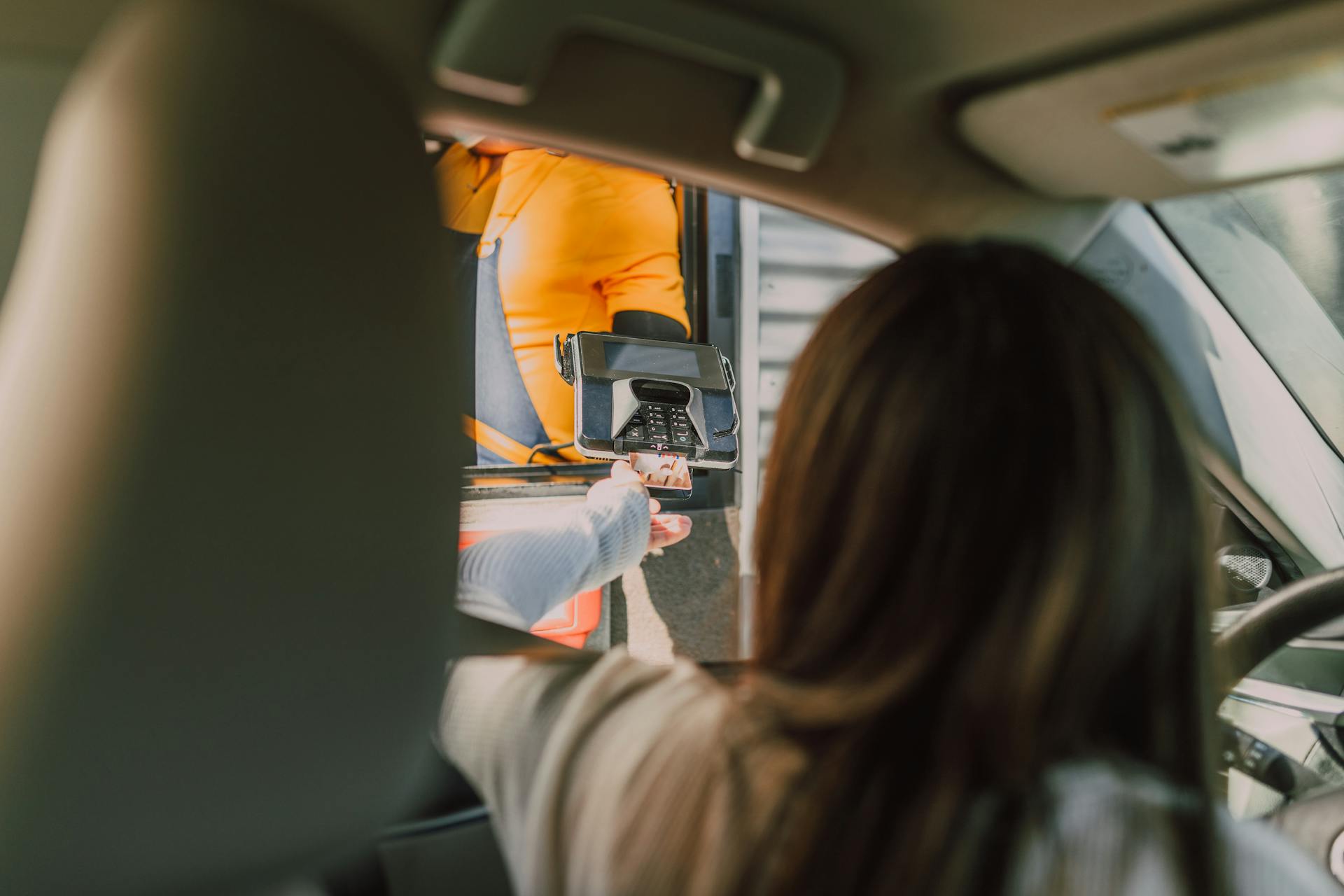 Eine Frau, die in ihrem Auto sitzt und an einem Drive-Through bezahlt | Quelle: Pexels