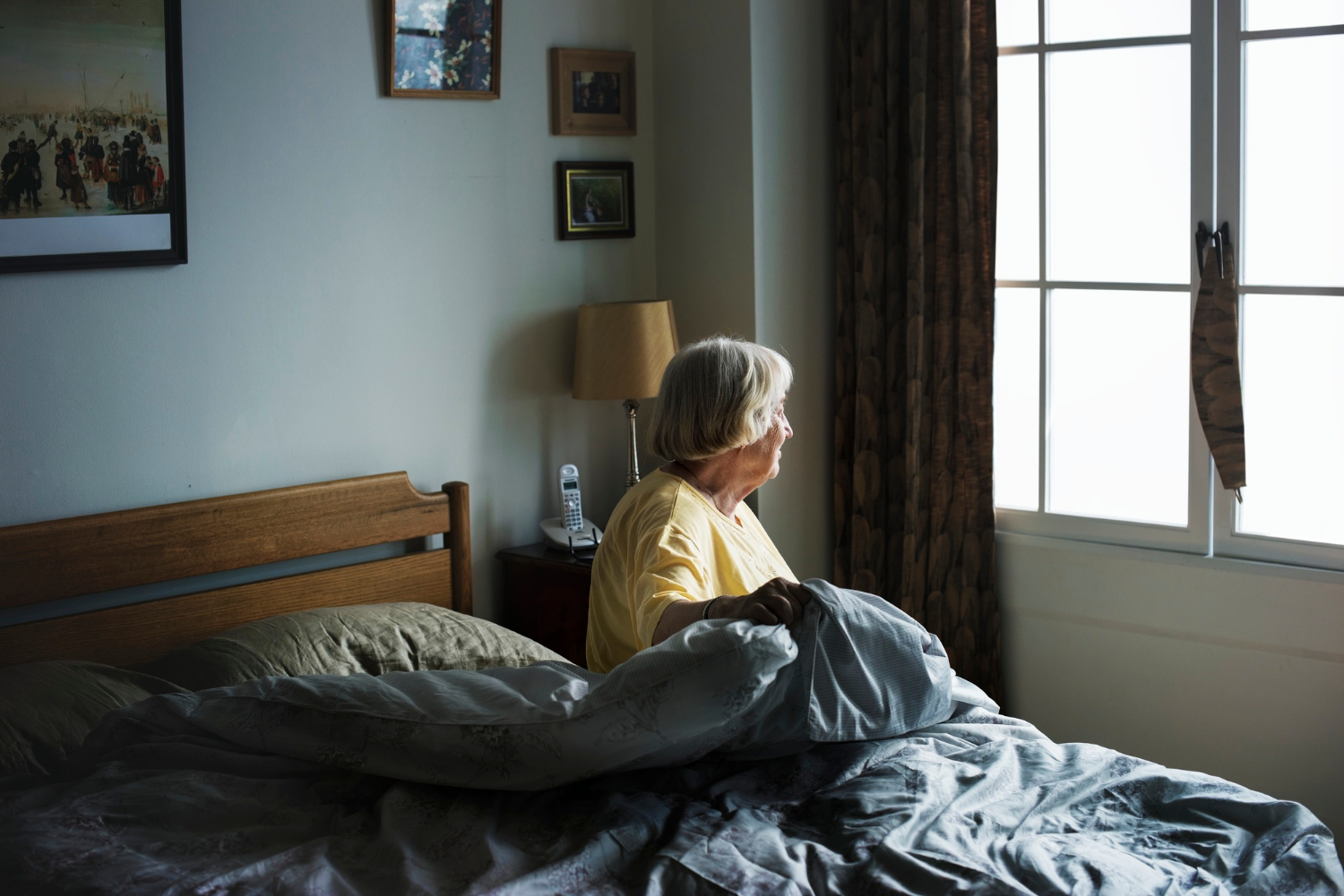 Eine einsame ältere Frau, die auf ihrem Bett sitzt und aus dem Fenster starrt | Quelle: Freepik