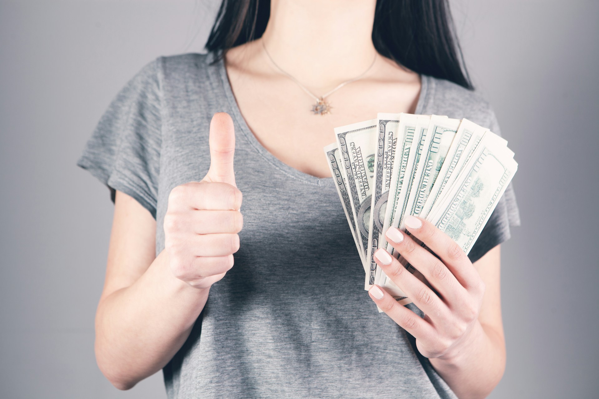 Eine Frau hält Geld in der Hand und zeigt den Daumen nach oben | Quelle: Unsplash