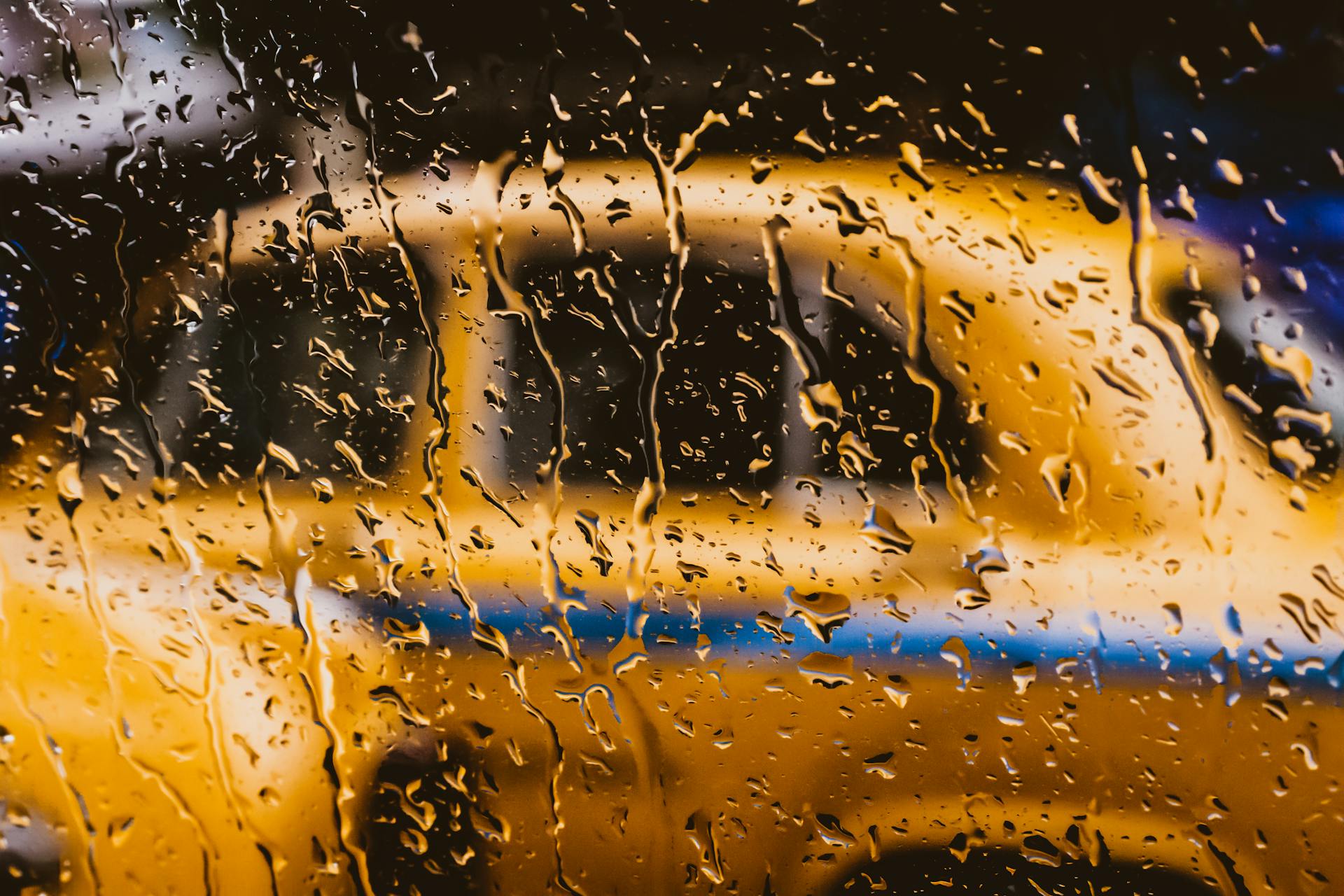 Ein nasses Fenster mit einem verschwommenen gelben Auto dahinter | Quelle: Pexels
