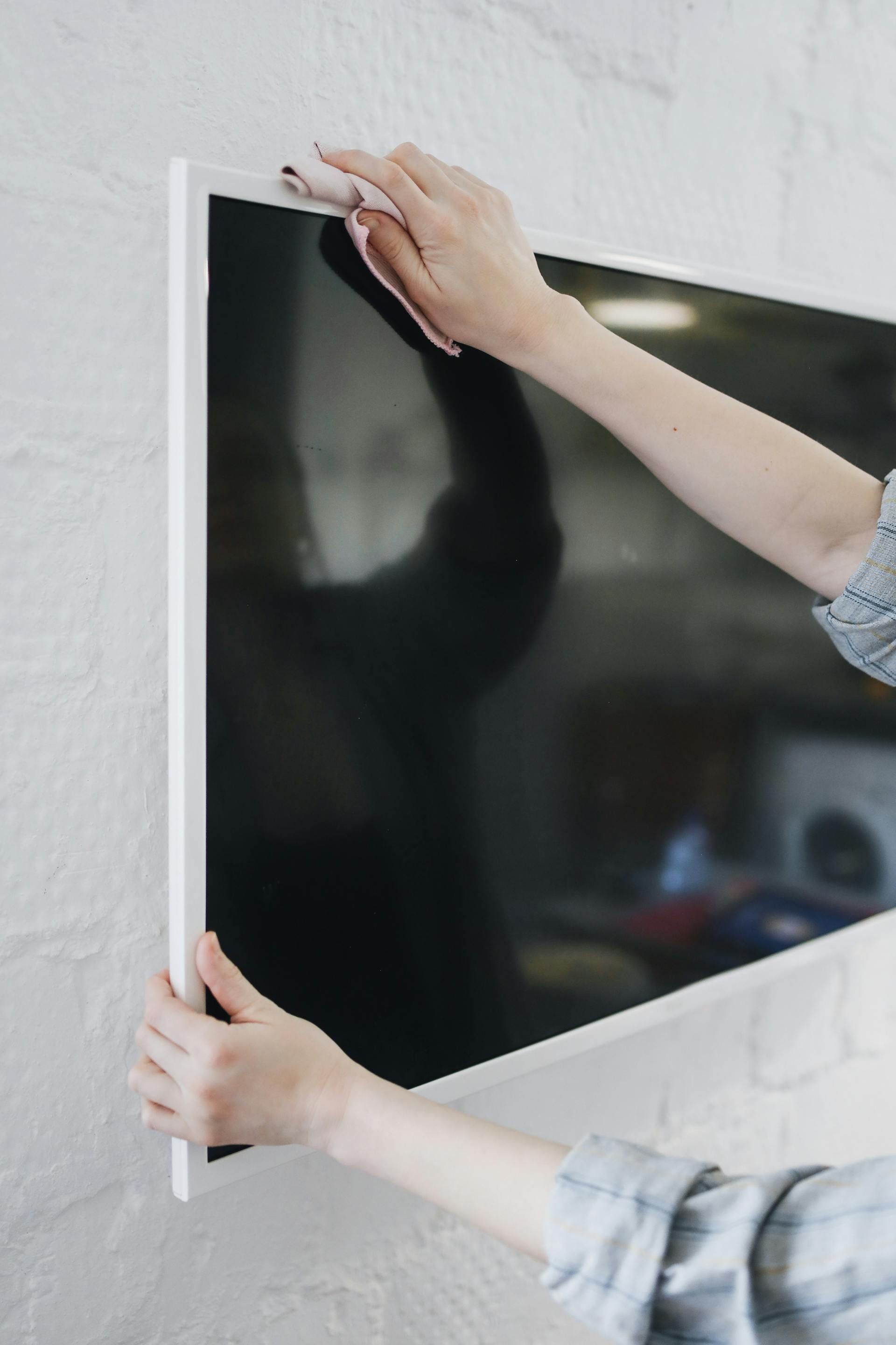 Eine Nahaufnahme einer Person, die einen an der Wand montierten Fernseher abwischt | Quelle: Pexels