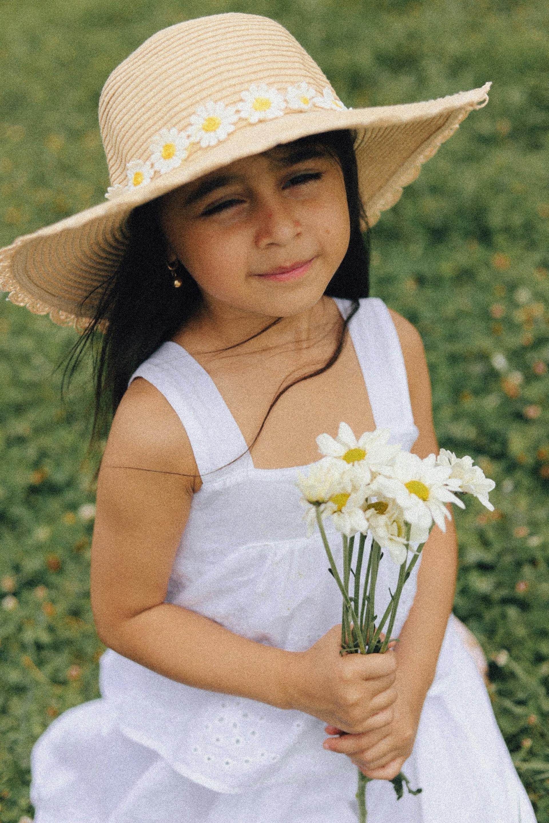 Ein kleines Mädchen in einem weißen Kleid und einem Strohhut mit Gänseblümchen hält einen Blumenstrauß | Quelle: Pexels