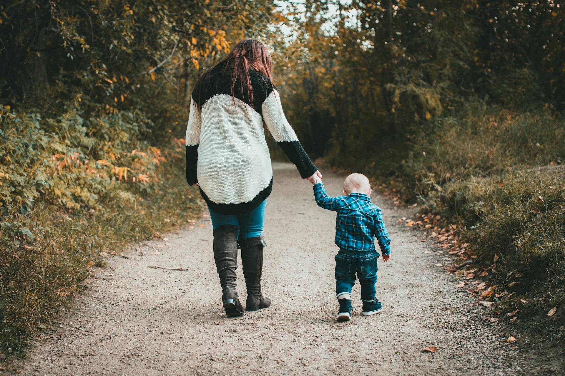 Eine Frau hält die Hand ihres kleinen Sohnes, während sie zusammen spazieren gehen | Quelle: Pexels