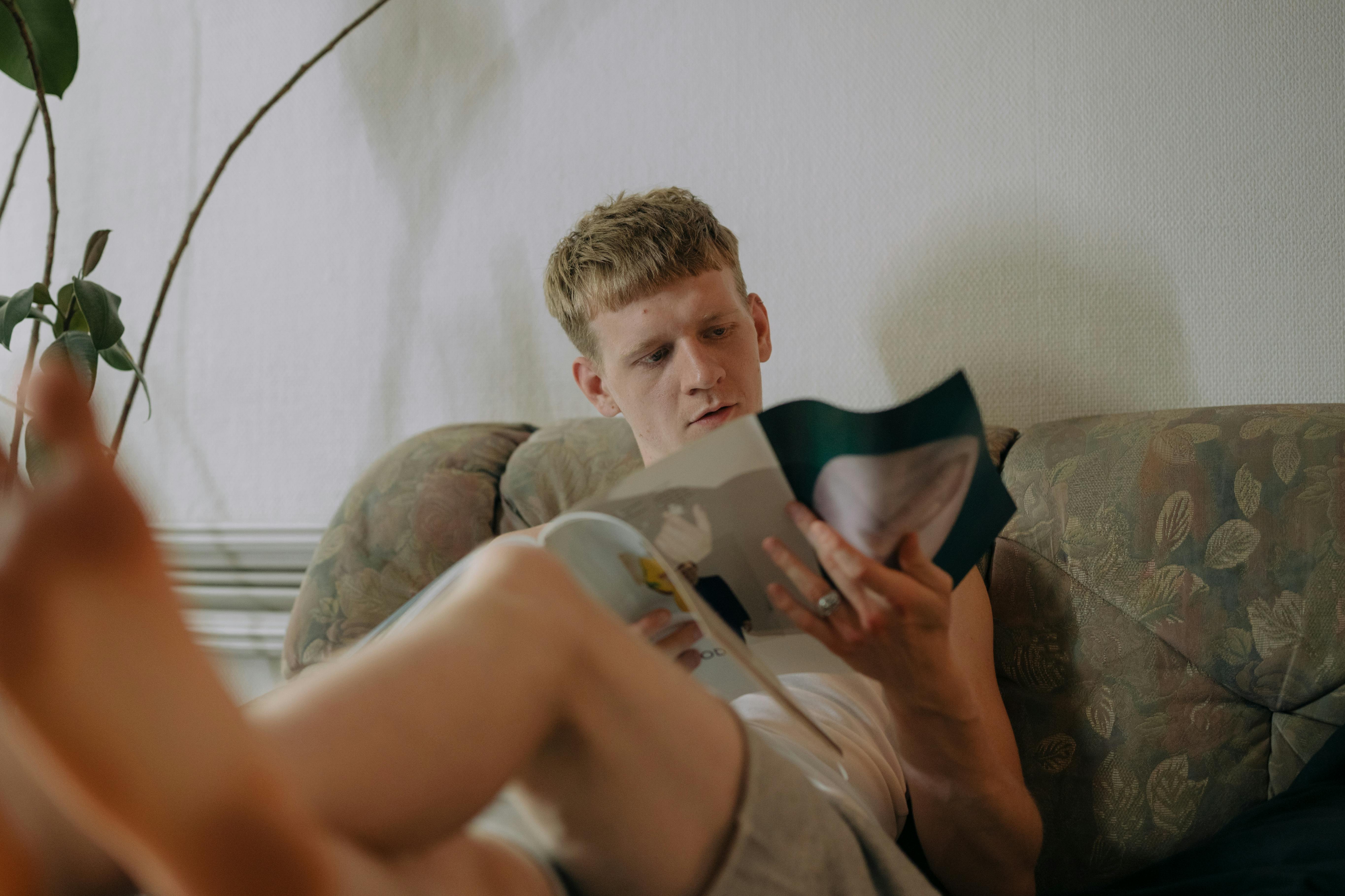 Mann, der auf dem Sofa sitzt und eine Zeitschrift liest | Quelle: Pexels