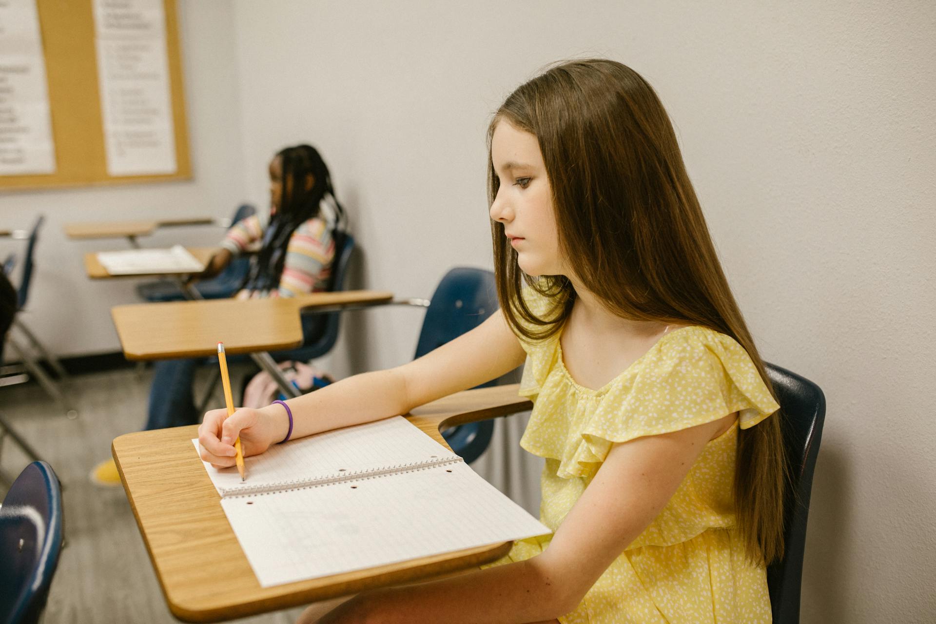 Ein verzweifeltes Mädchen sitzt in ihrem Klassenzimmer und schreibt in ihr Notizbuch | Quelle: Pexels