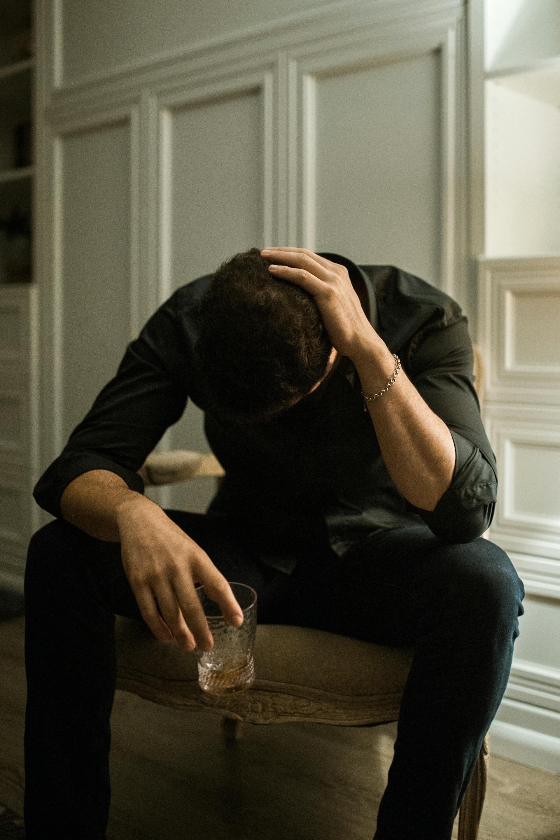 Ein verzweifelter Mann sitzt mit gesenktem Kopf und hält ein Glas in der Hand | Quelle: Pexels