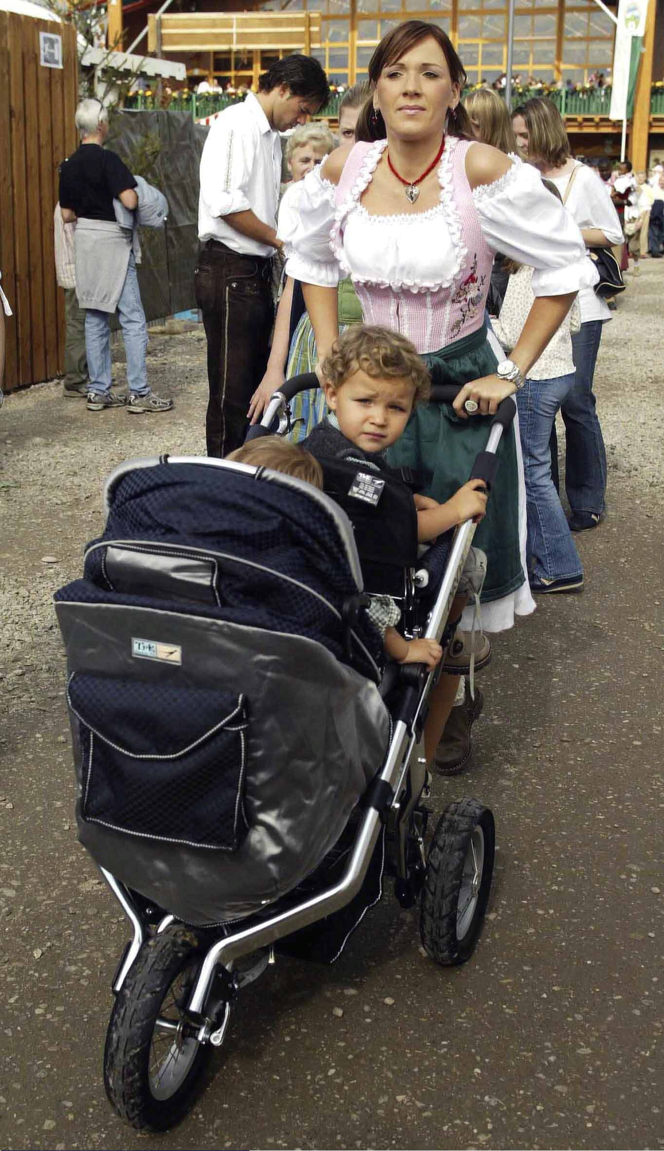 Michael Ballack (im Hintergrund) schreibt Autogramme während seine Ehefrau Simone den Kinderwagen mit den Kindern Louis und Emilio schiebt, 2004 | Quelle: Getty Images