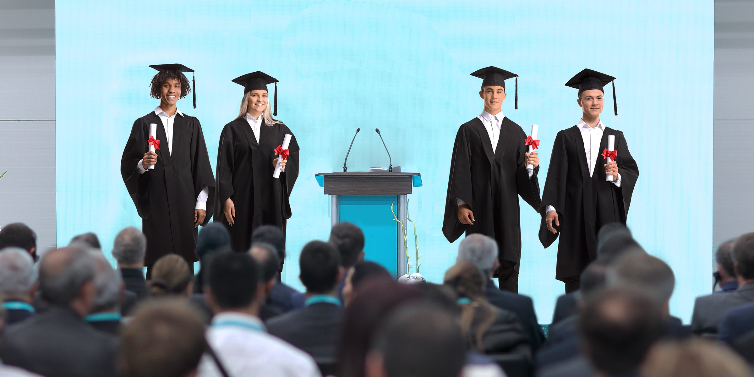 Absolventen in Kappe und Talar halten stolz ihre Diplome auf der Bühne, während das Publikum zuschaut | Quelle: Shutterstock