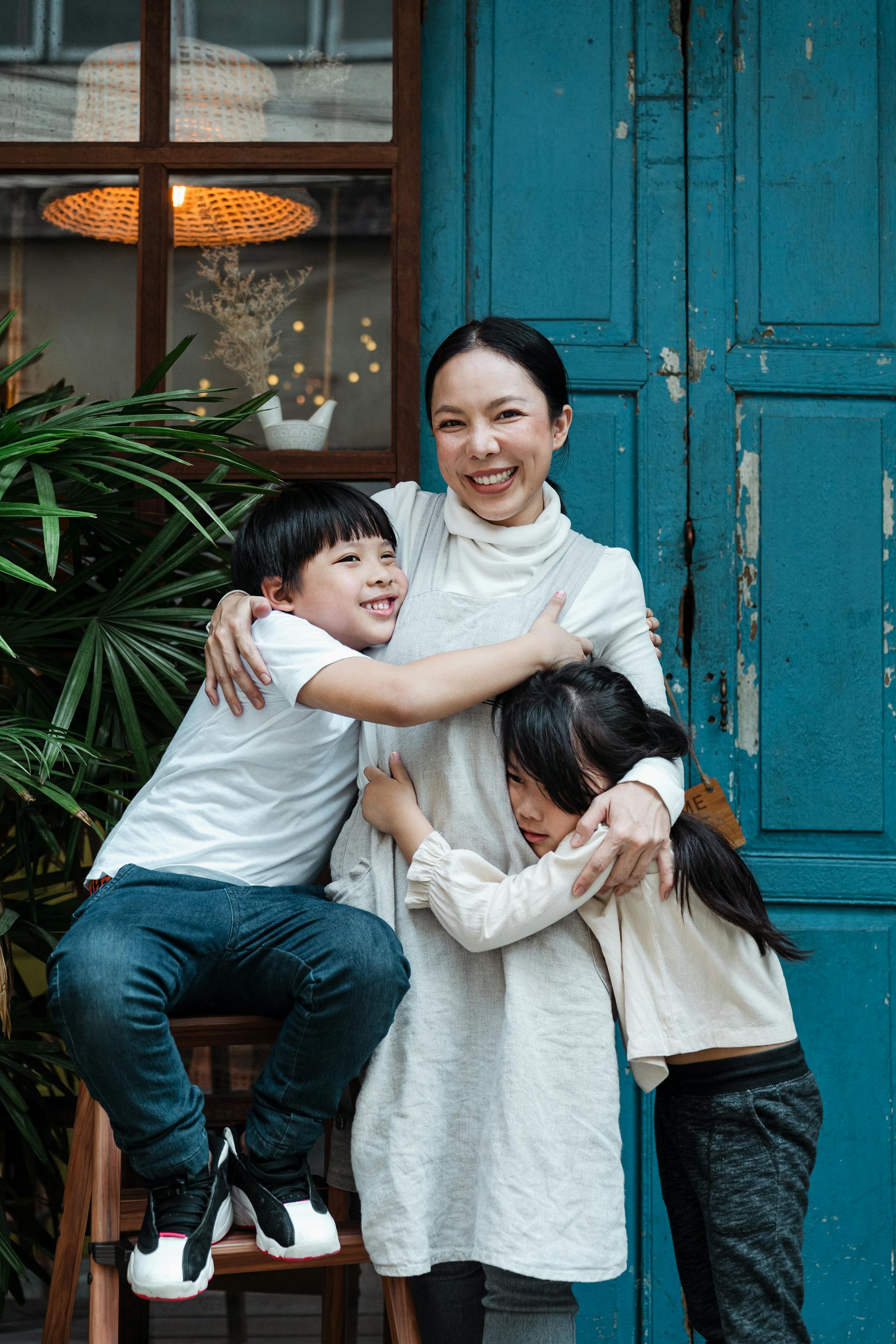 Eine glückliche Mutter, die ihre beiden Kinder umarmt, während sie vor einer blauen Tür steht | Quelle: Pexels