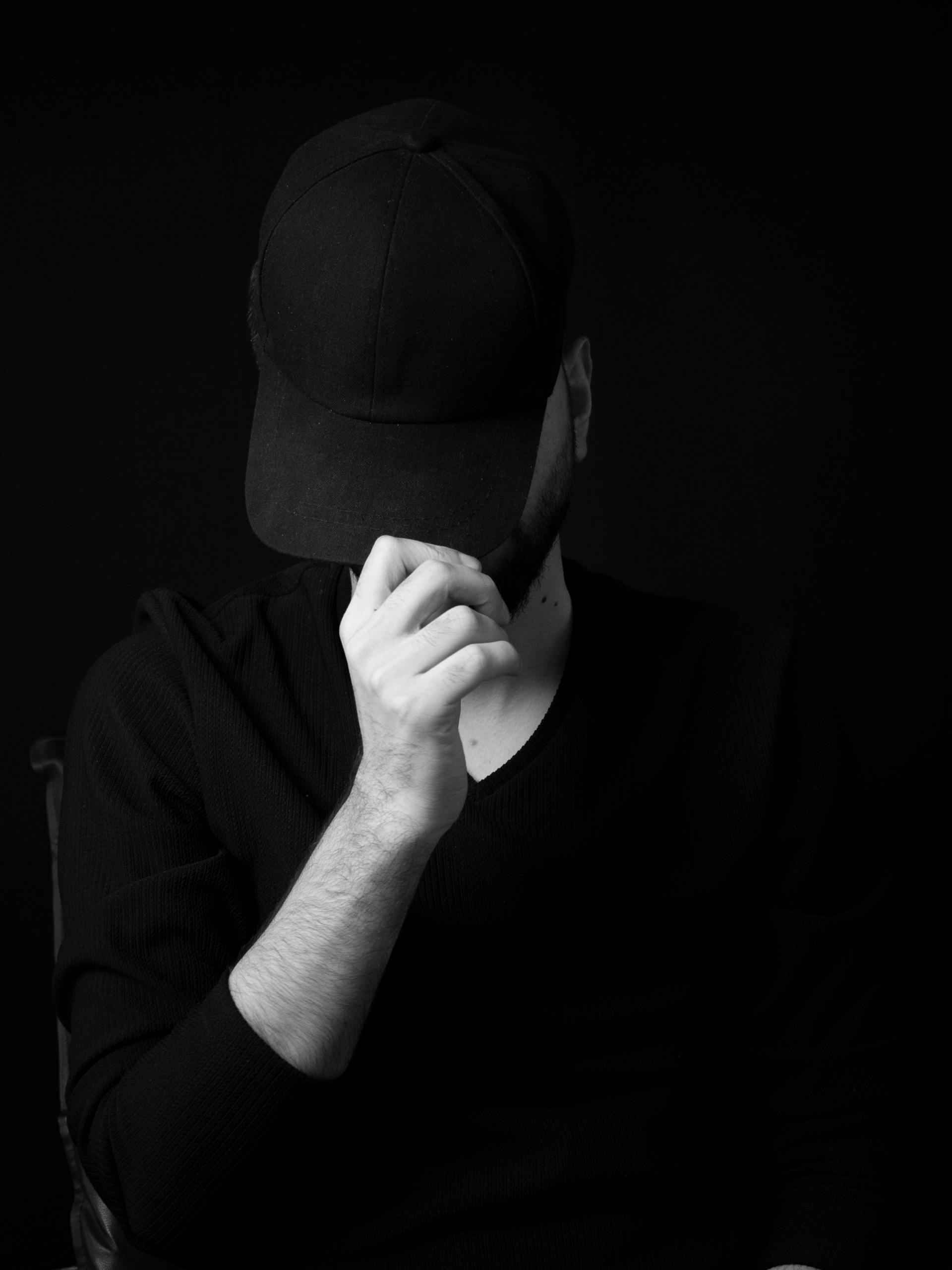 Graustufenfoto eines Mannes, der sein Gesicht mit seiner Mütze verdeckt | Quelle: Pexels